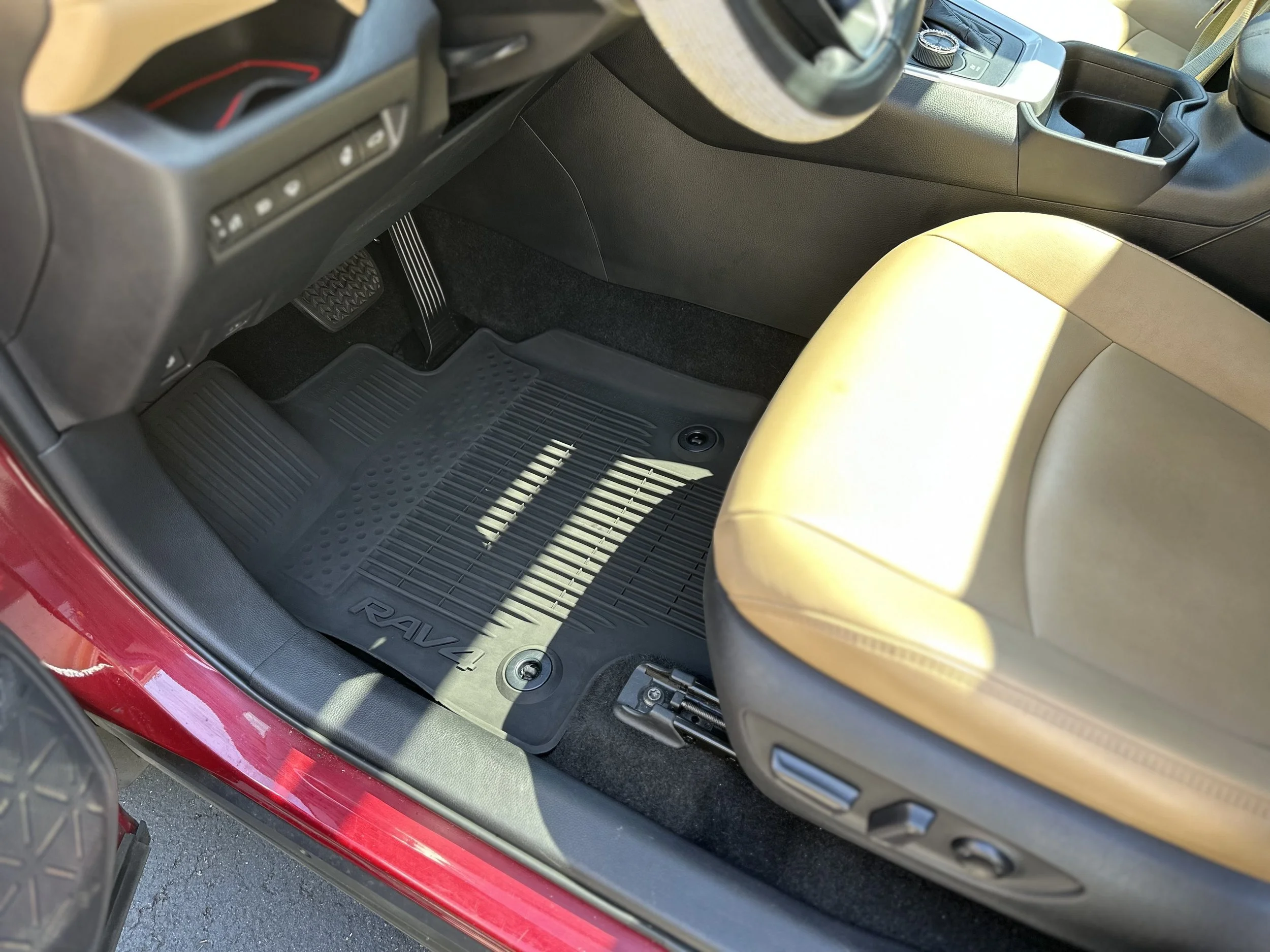 Front passenger side of a red Toyota RAV4, showing a tan leather seat and a black rubber floor mat with the RAV4 logo.