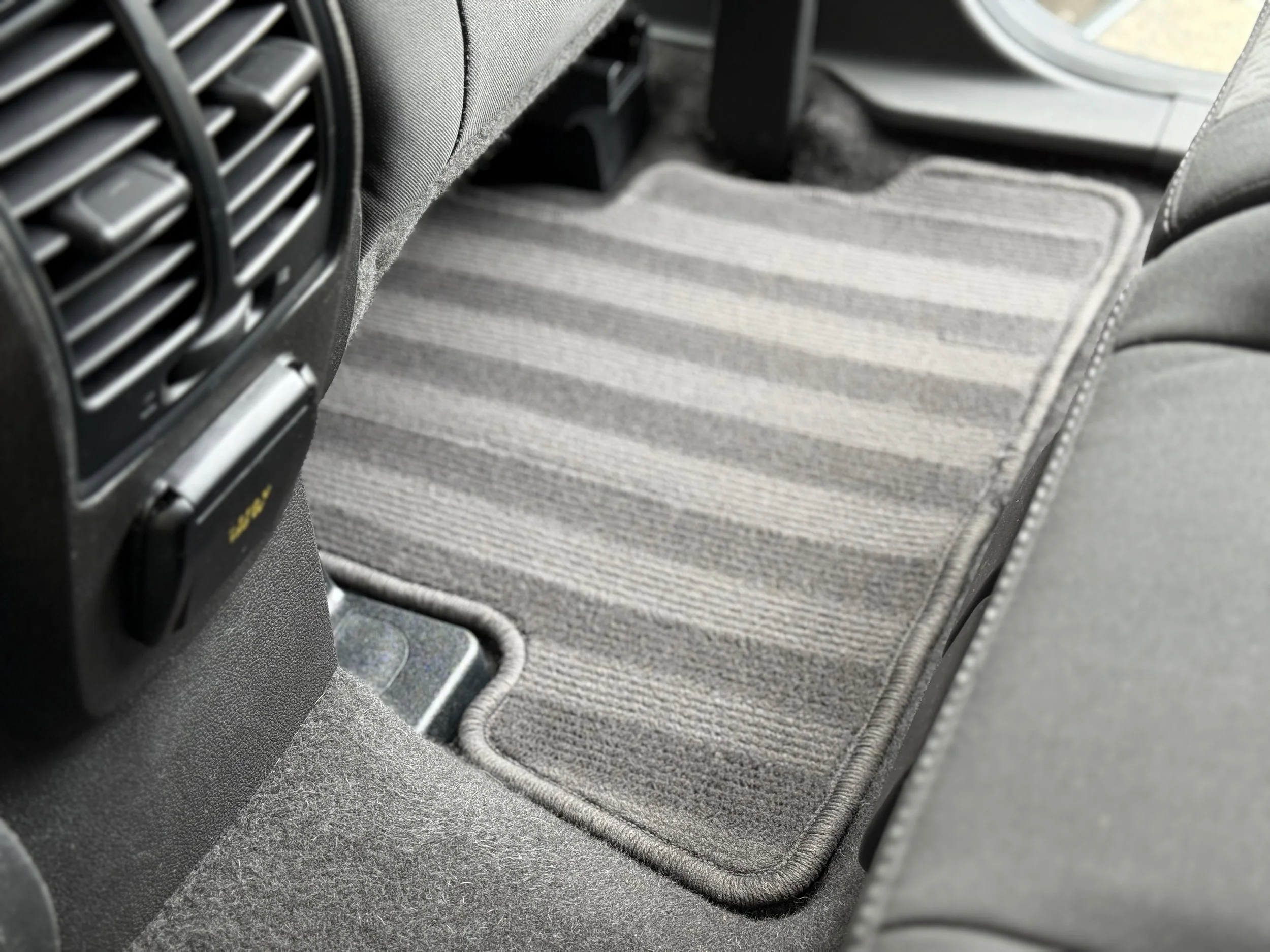 View of the interior of a vehicle showing a gray striped floor mat, air vents, and part of the back of the front seats.