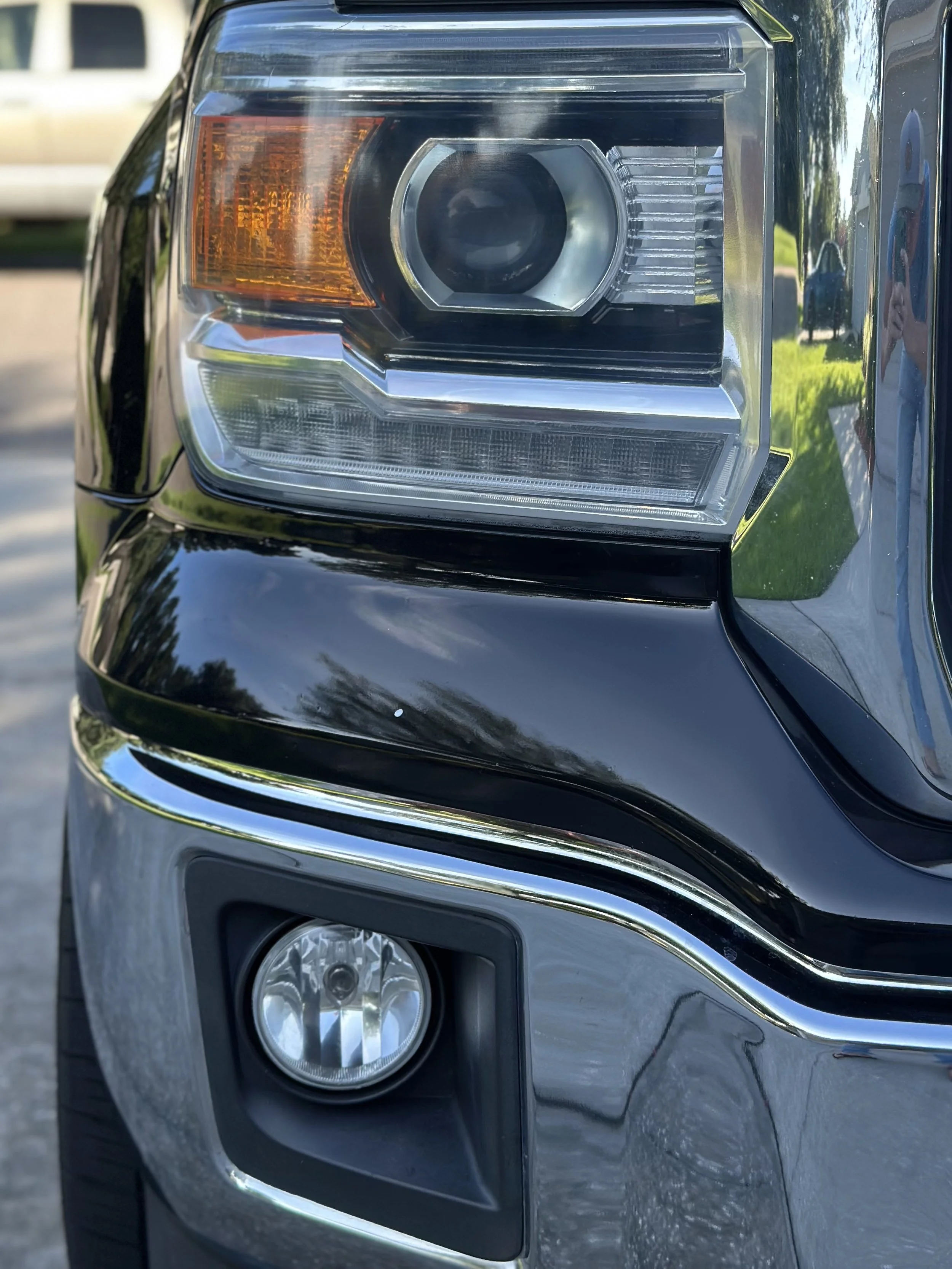 Close-up of the front headlight and fog light of a black vehicle reflected in its shiny surface after headlight restoration