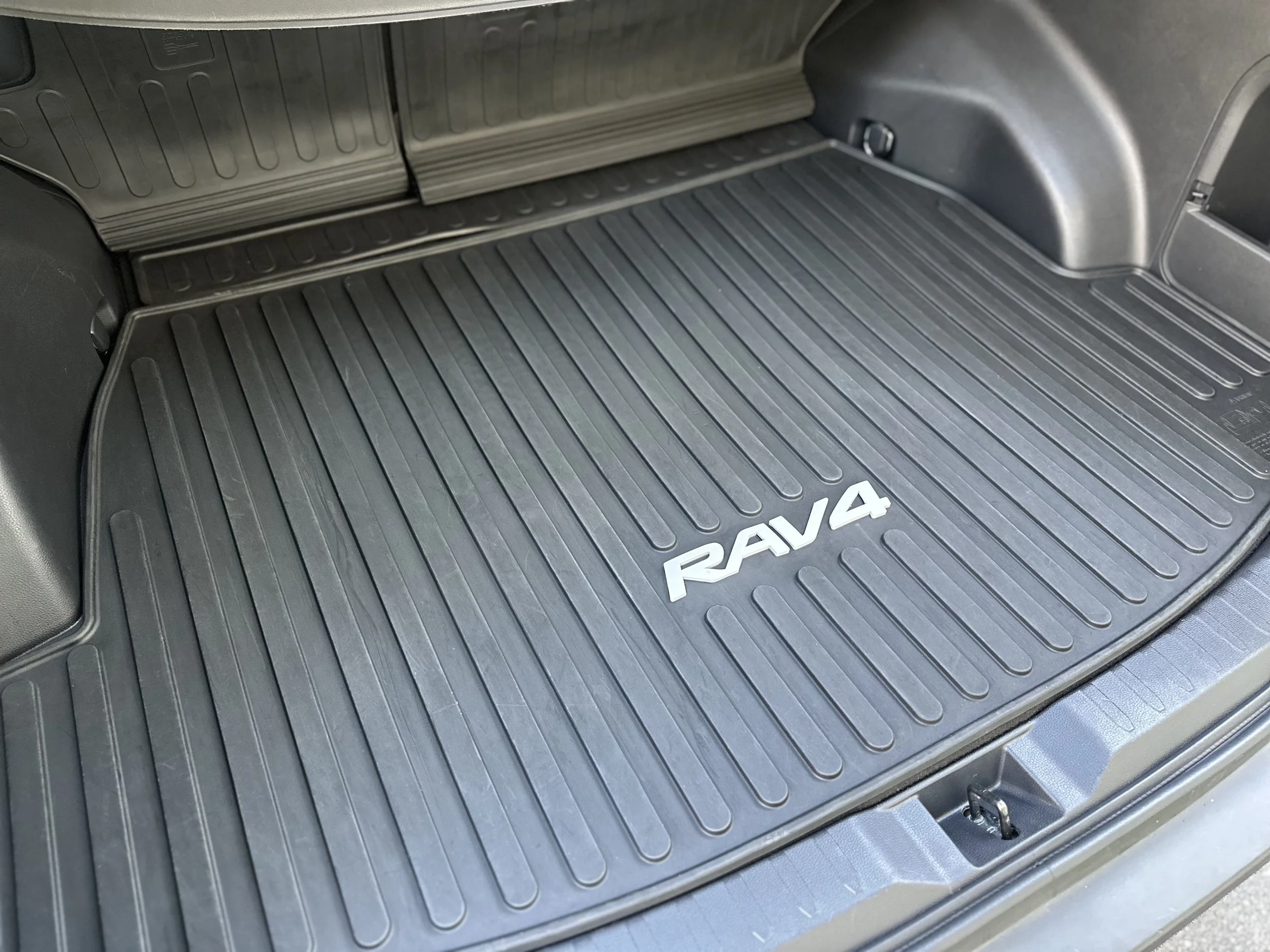 Car trunk with a black rubber mat and the word 'RAV4' in white letters.