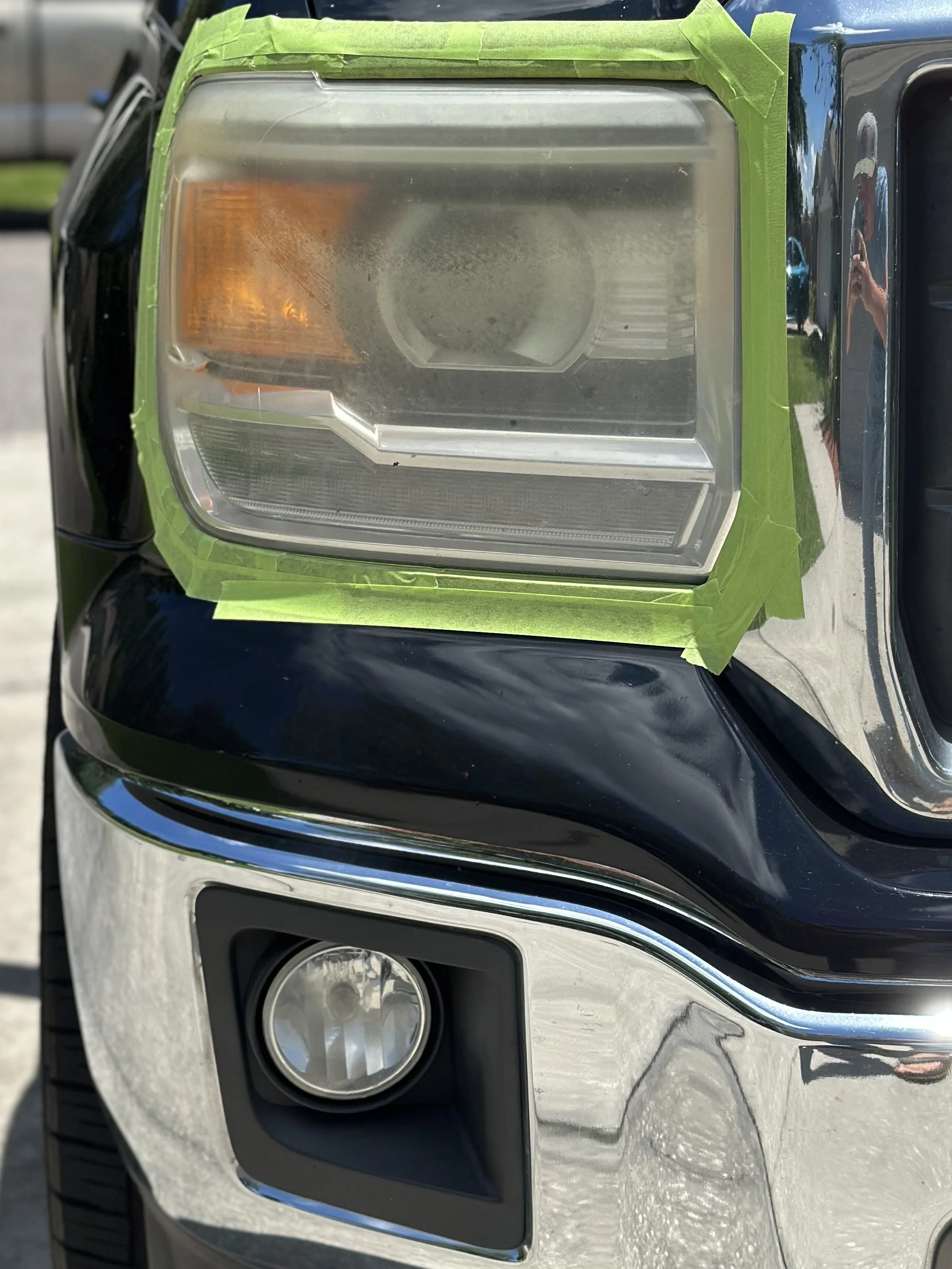 Close-up of a vehicle's headlight with protective tape around it, undergoing headlight restoration