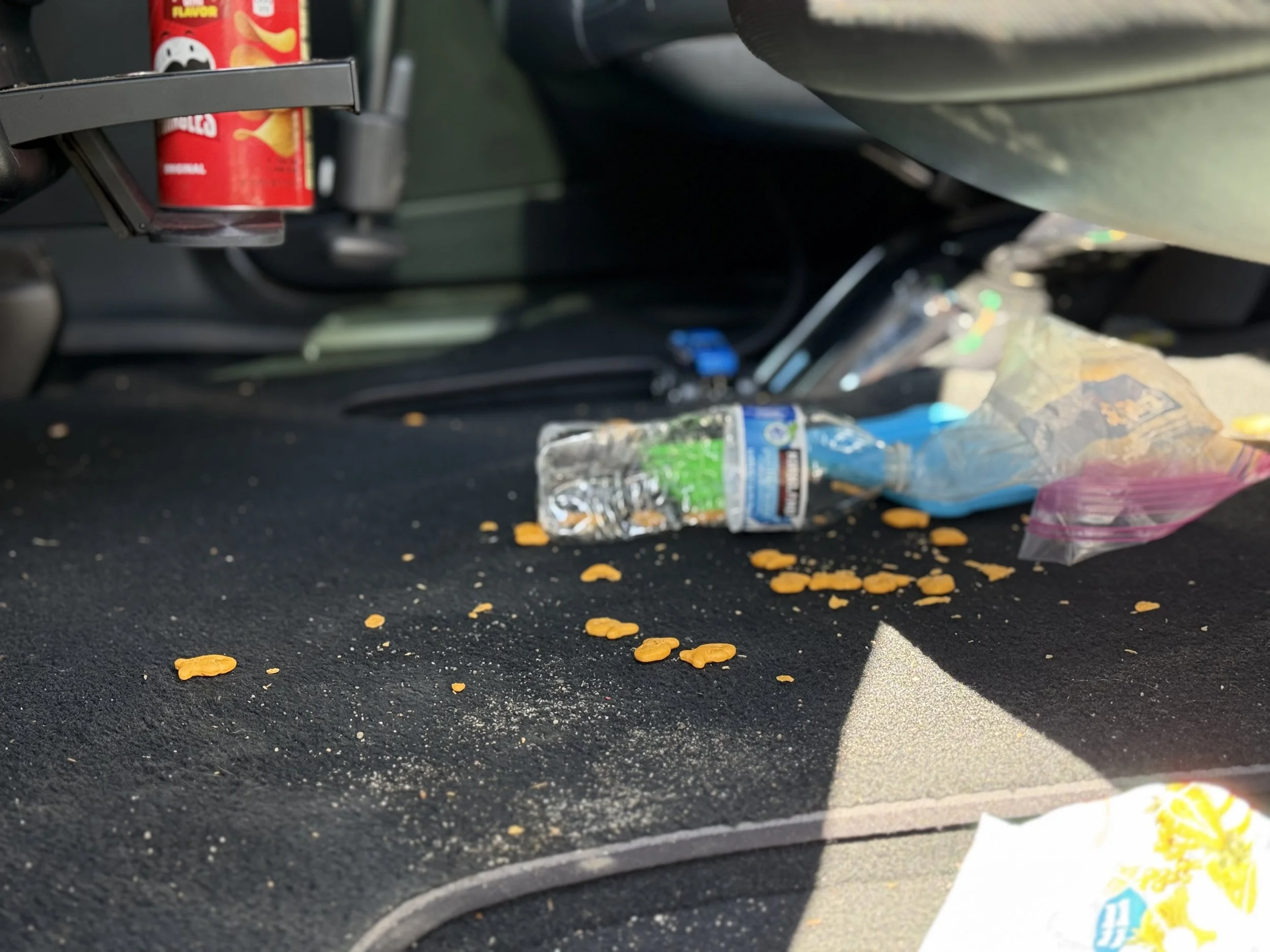 Messy car floor with spilled snacks, an empty water bottle, and trash.