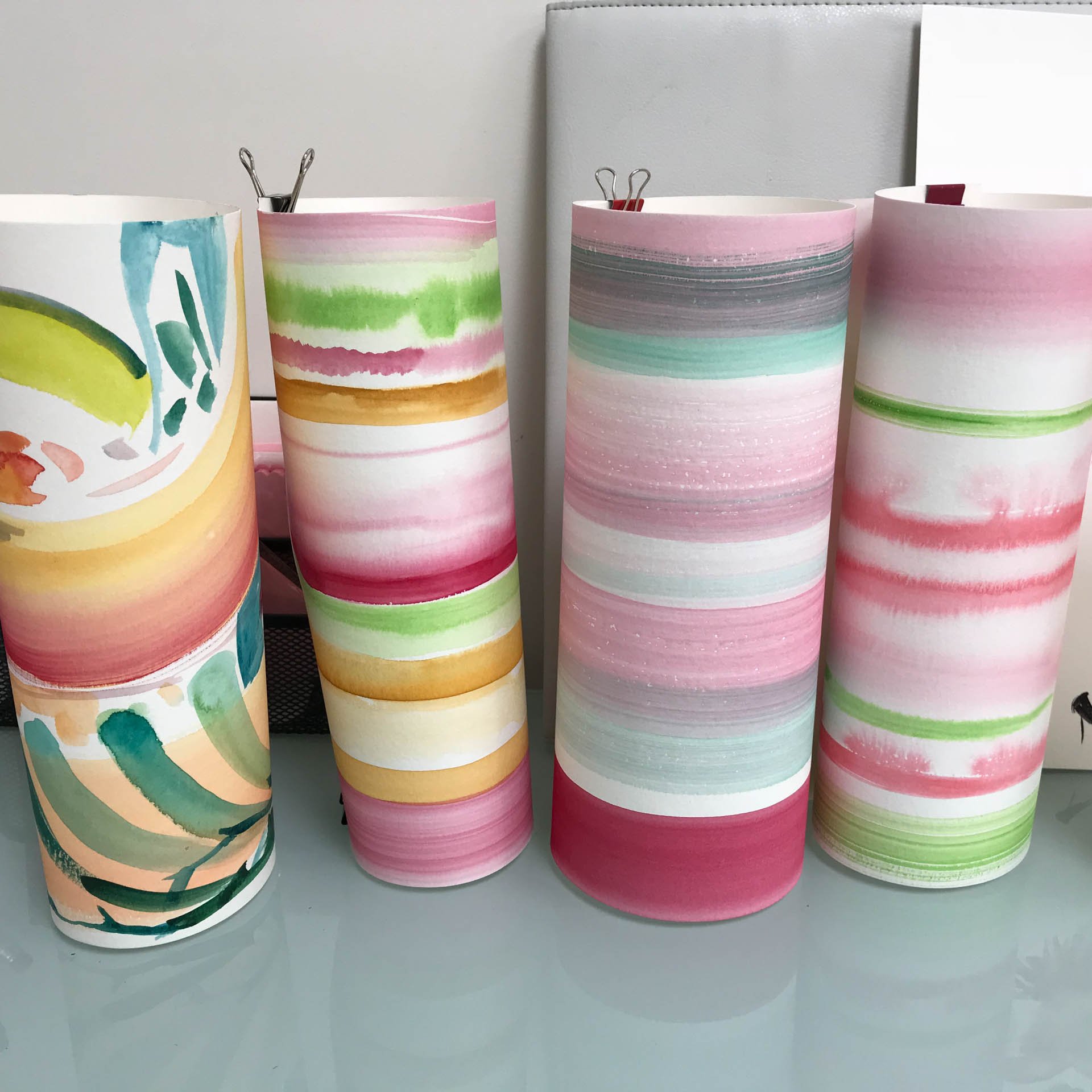 Hand painted abstract watercolor-style horizontal stripes in shades of pink, green, yellow, gray, and blue, placed on a flat surface against a light-colored background.
