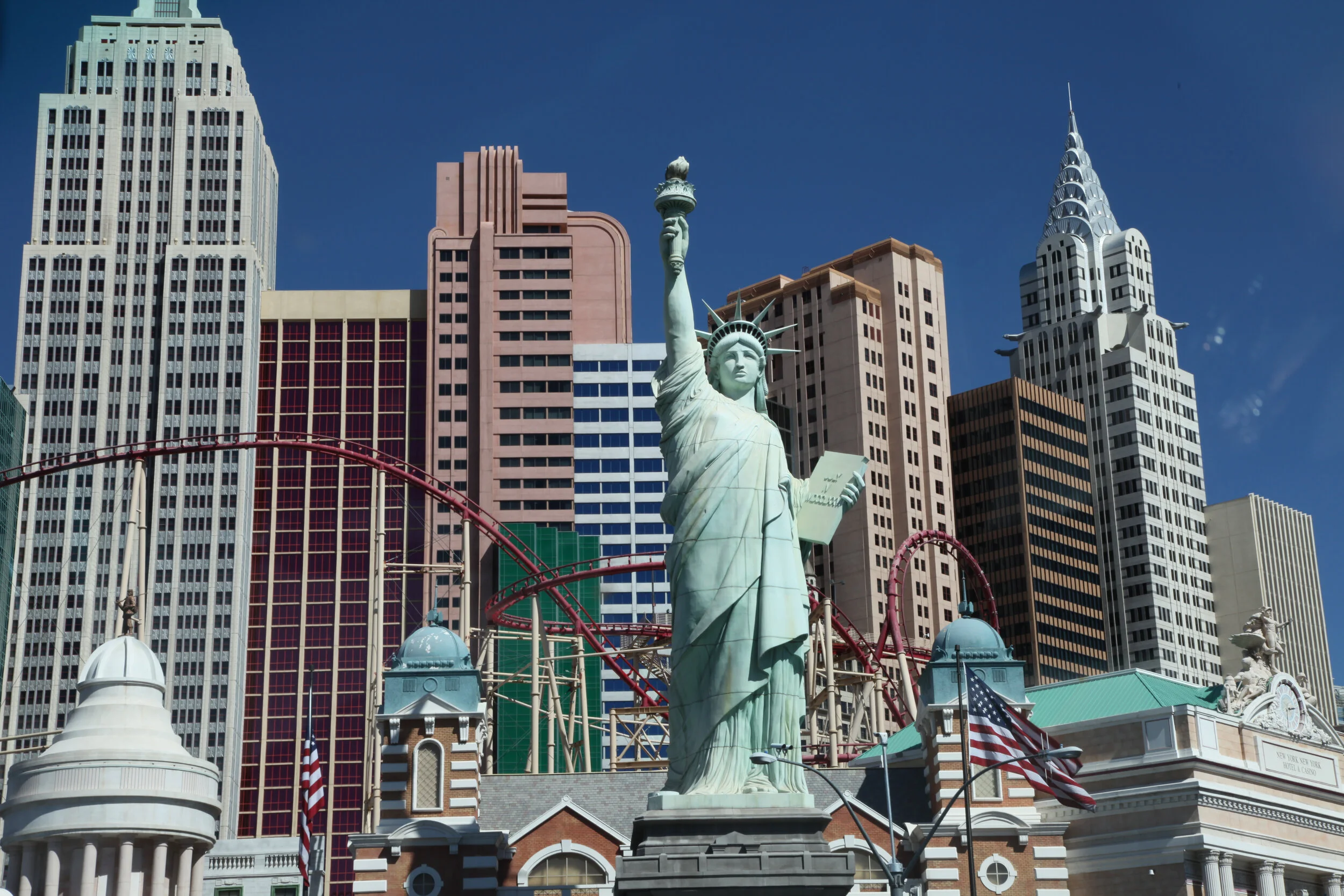 Replica of the Statue of Liberty in front of a cityscape with tall skyscrapers and a roller coaster behind