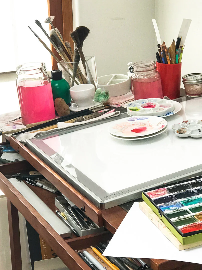 An artist's studio with brushes, paints, jars on a wooden table.