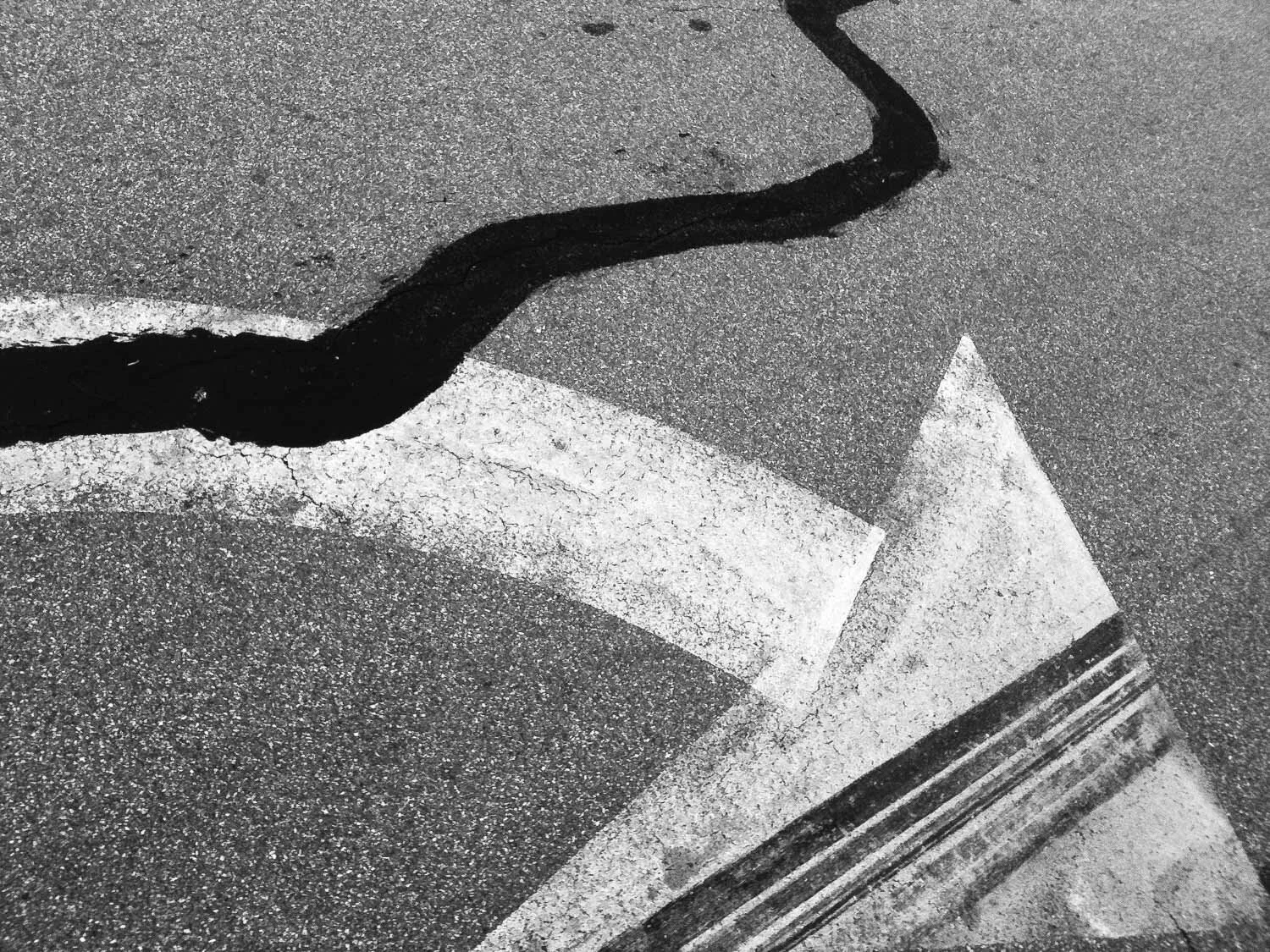 Black asphalt with white painted arrow and black painted winding line on a textured street surface.