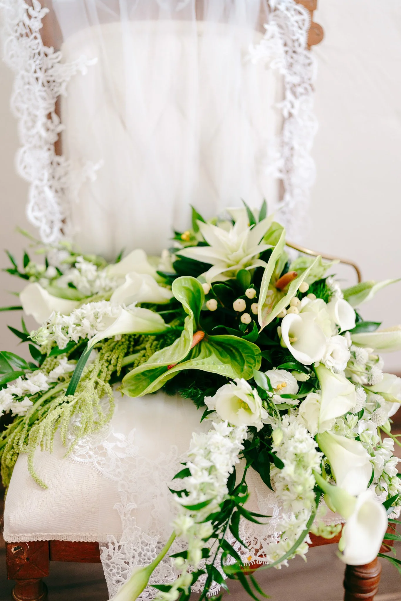 White floral arrangement on a lace-covered surface with a lace and wood chair in the background.