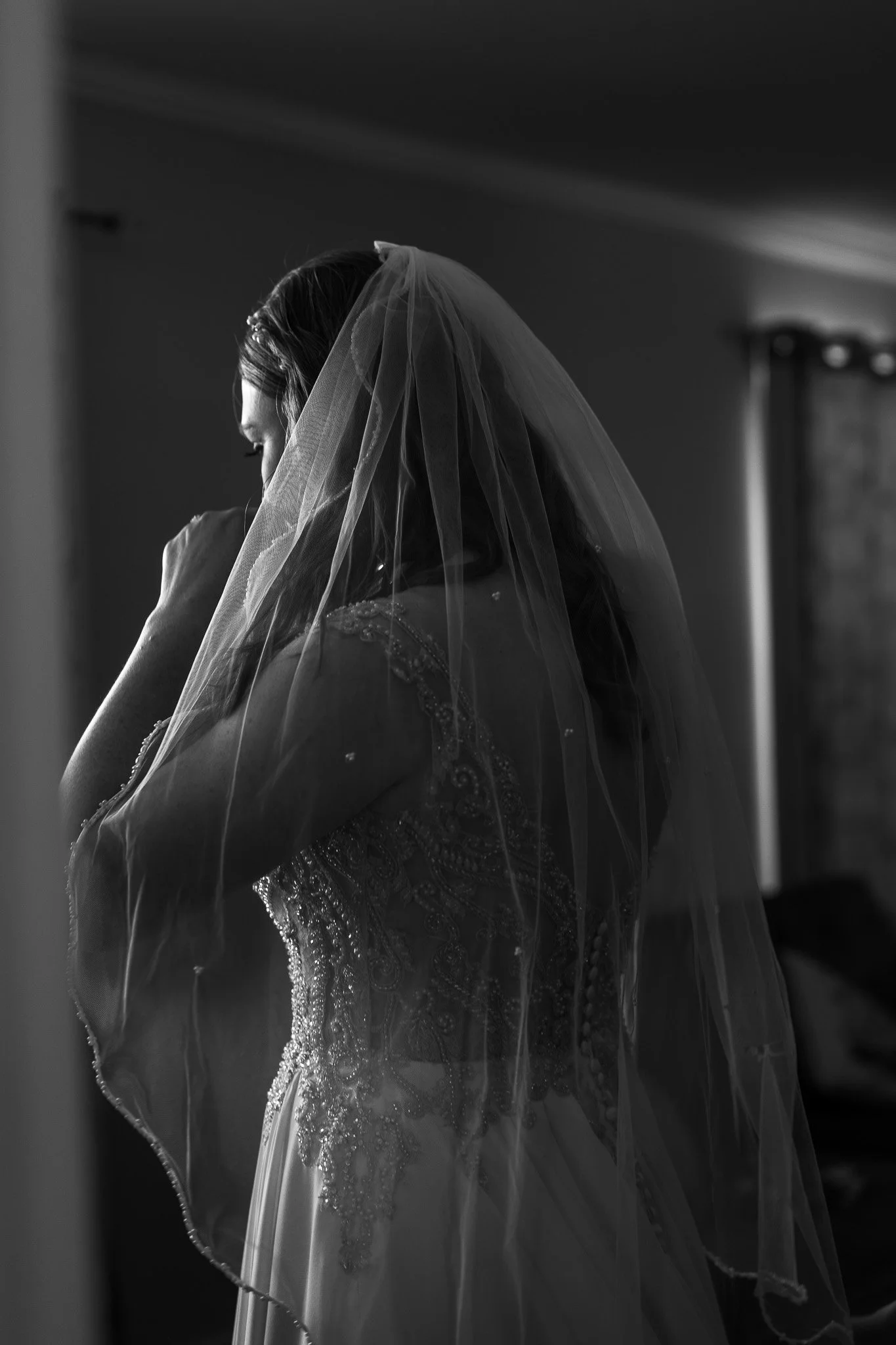 Black and white photo of a bride on her wedding day, wearing a veil and wedding dress, with her hand near her face.