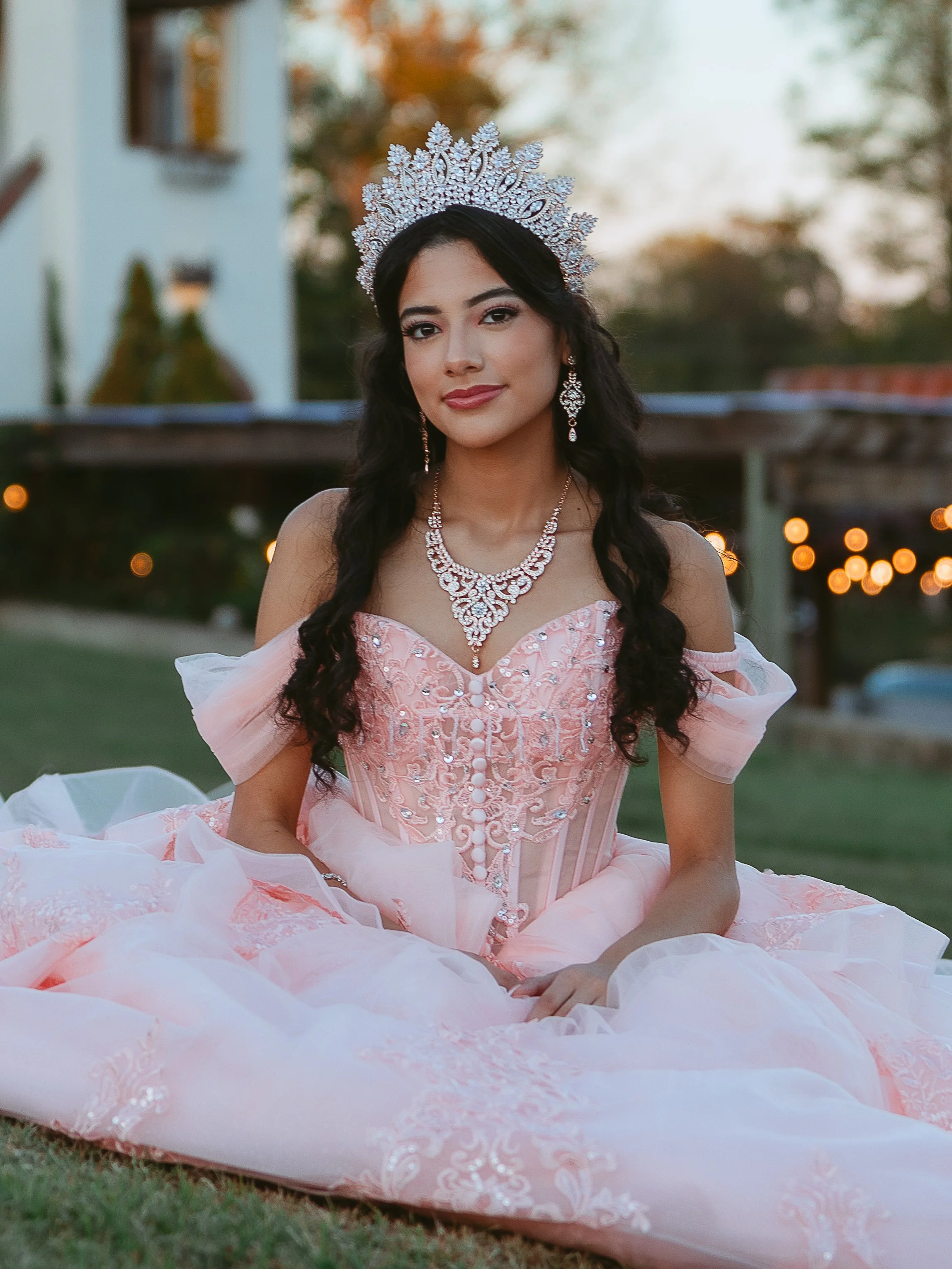 Teen girl in quinceañera gown and crown sitting in a field at Crown Winery, Humboldt, TN.