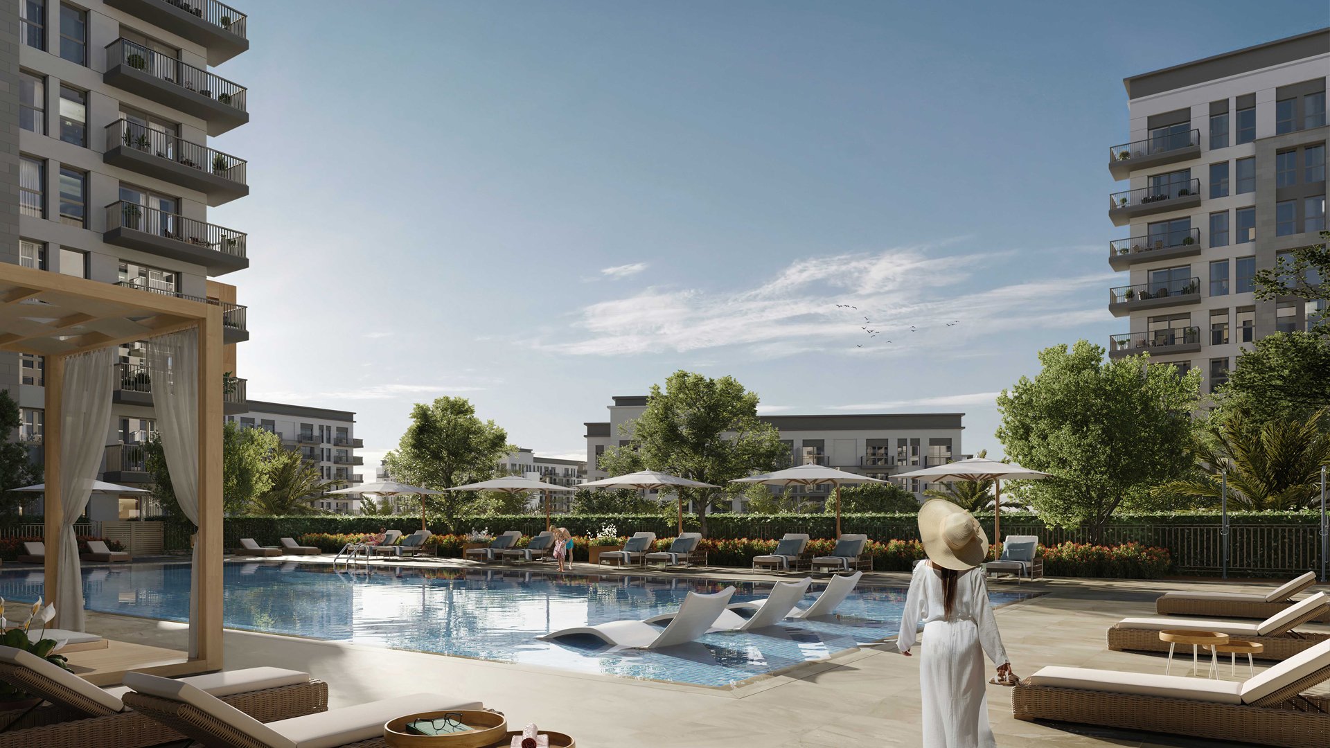 Modern apartment complex with a swimming pool area, lounge chairs, umbrellas, and surrounding greenery under a clear blue sky. Eagle Hills. Maryam Island CGI. Dubai Real estate marketing.