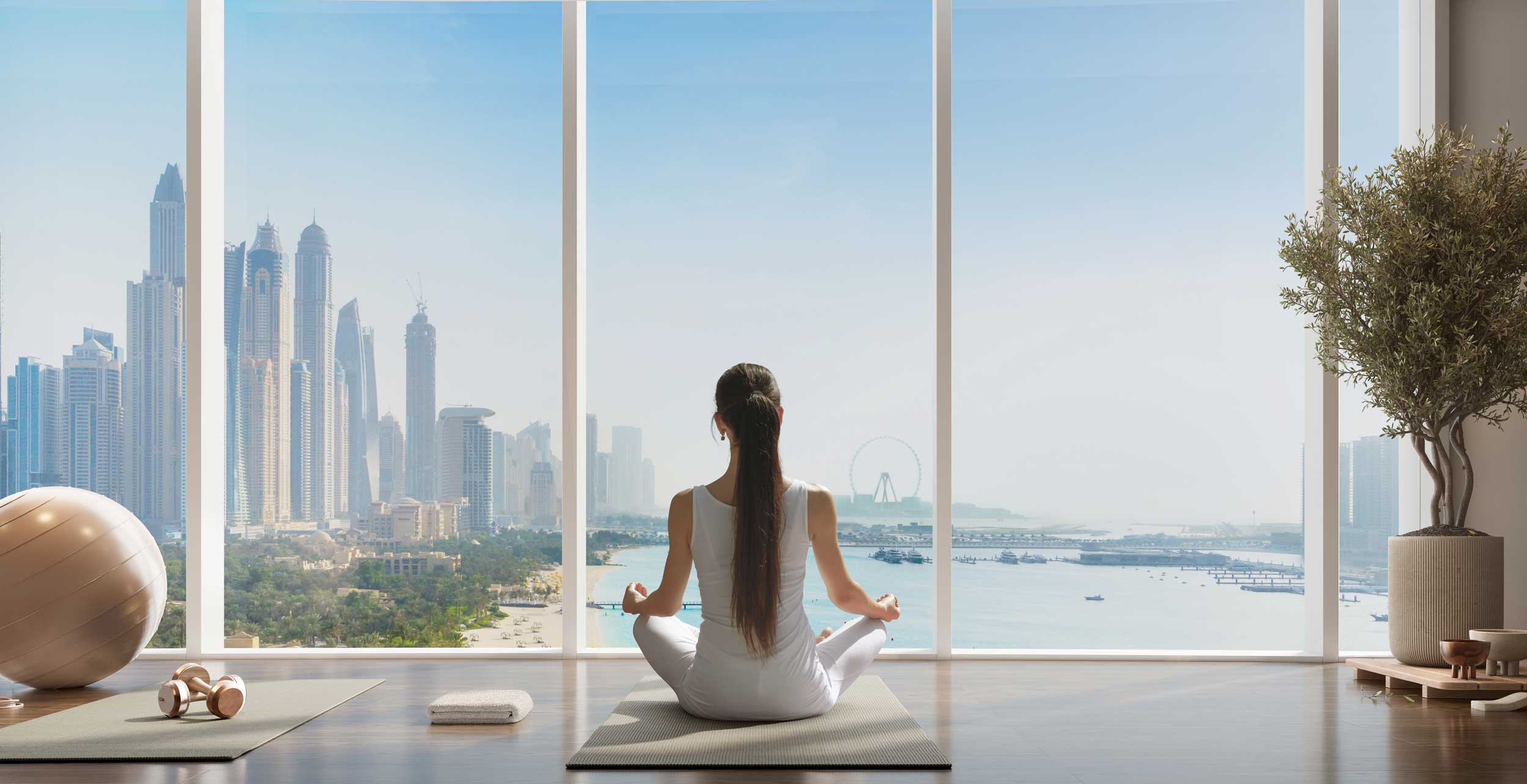 A woman with long dark hair practicing yoga in a white outfit in a bright room with floor-to-ceiling windows, overlooking a city skyline with skyscrapers, a river, and a Ferris wheel.