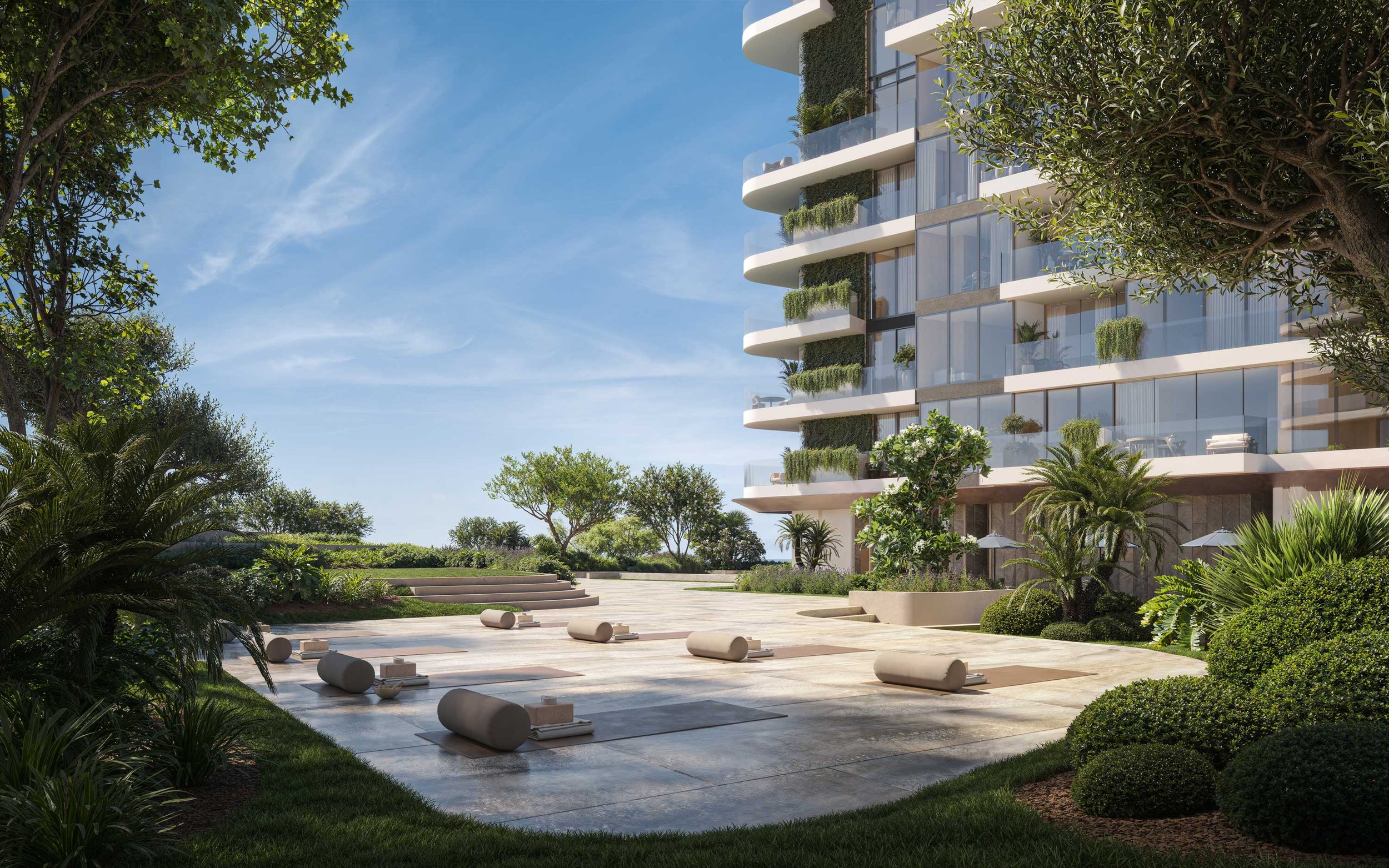 Outdoor yoga area with mats and bolsters in front of a modern apartment building, surrounded by lush green trees and plants, on sunny day.  Beyond Properties. Dubai Real Estate Marketing.