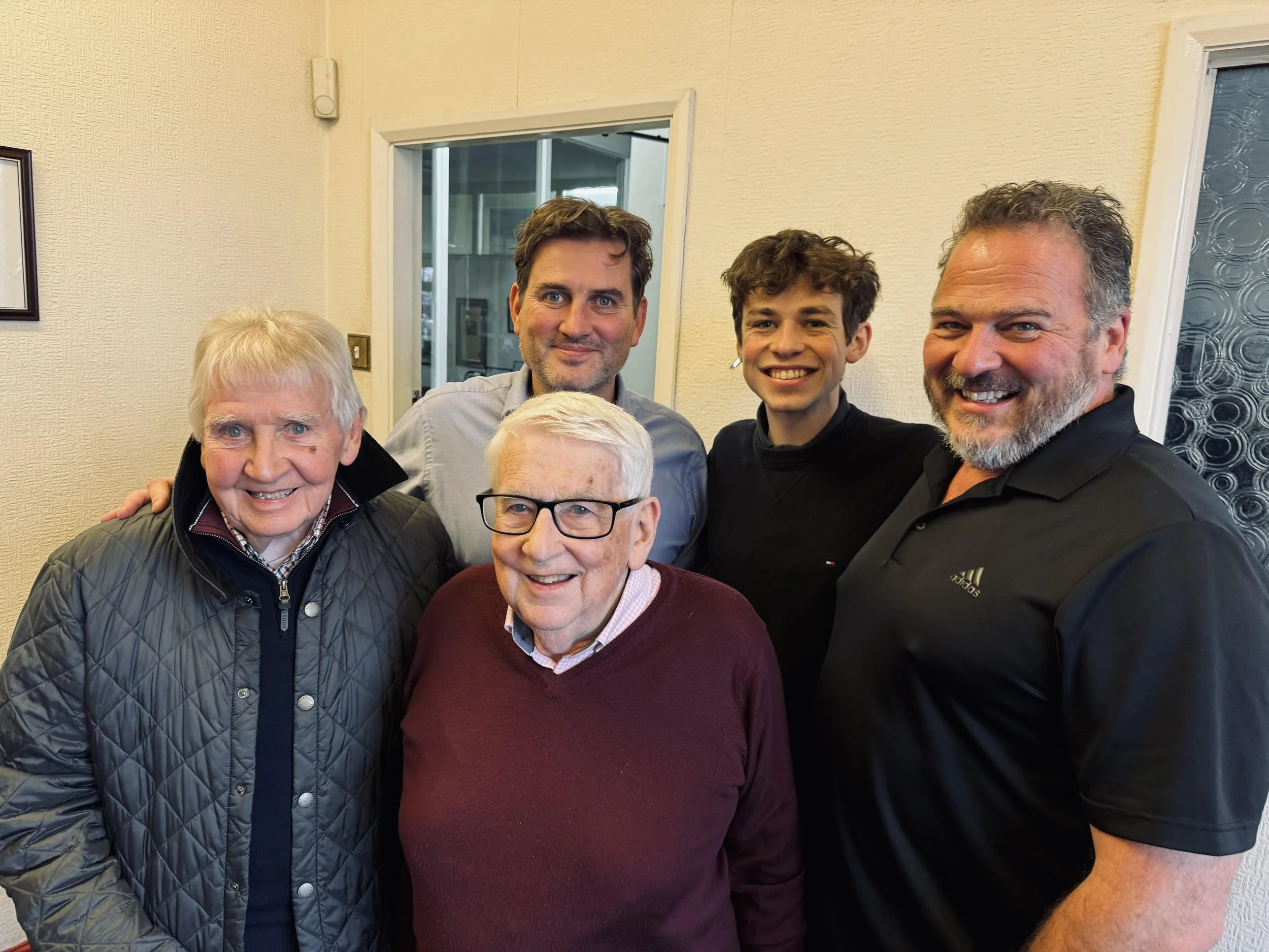 Six members of the Hill family of varying ages smiling and posing for a group photo indoors.