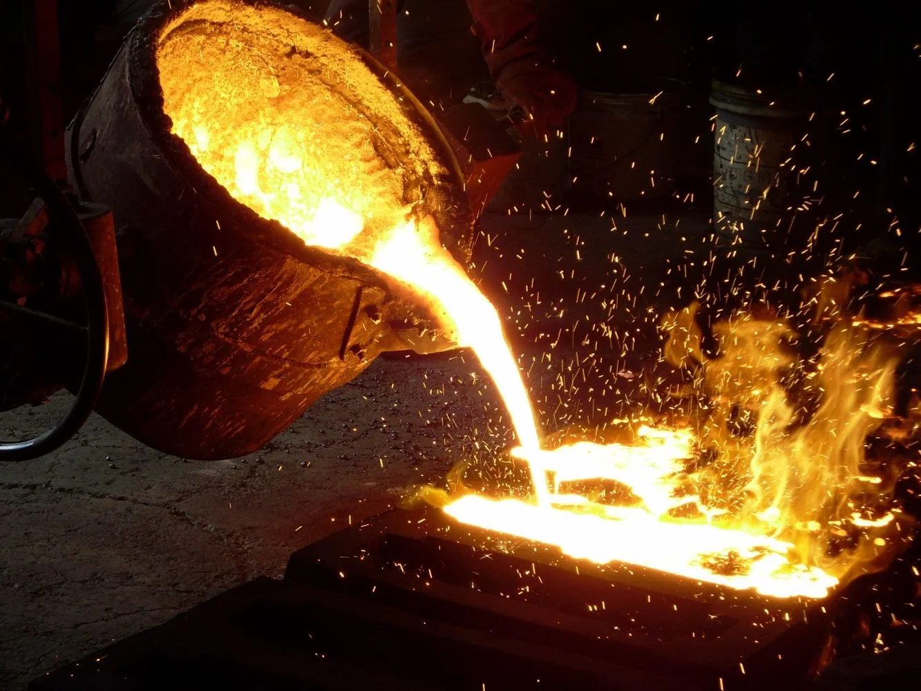 Molten metal being poured from a crucible into a mold during metal casting process with sparks flying.