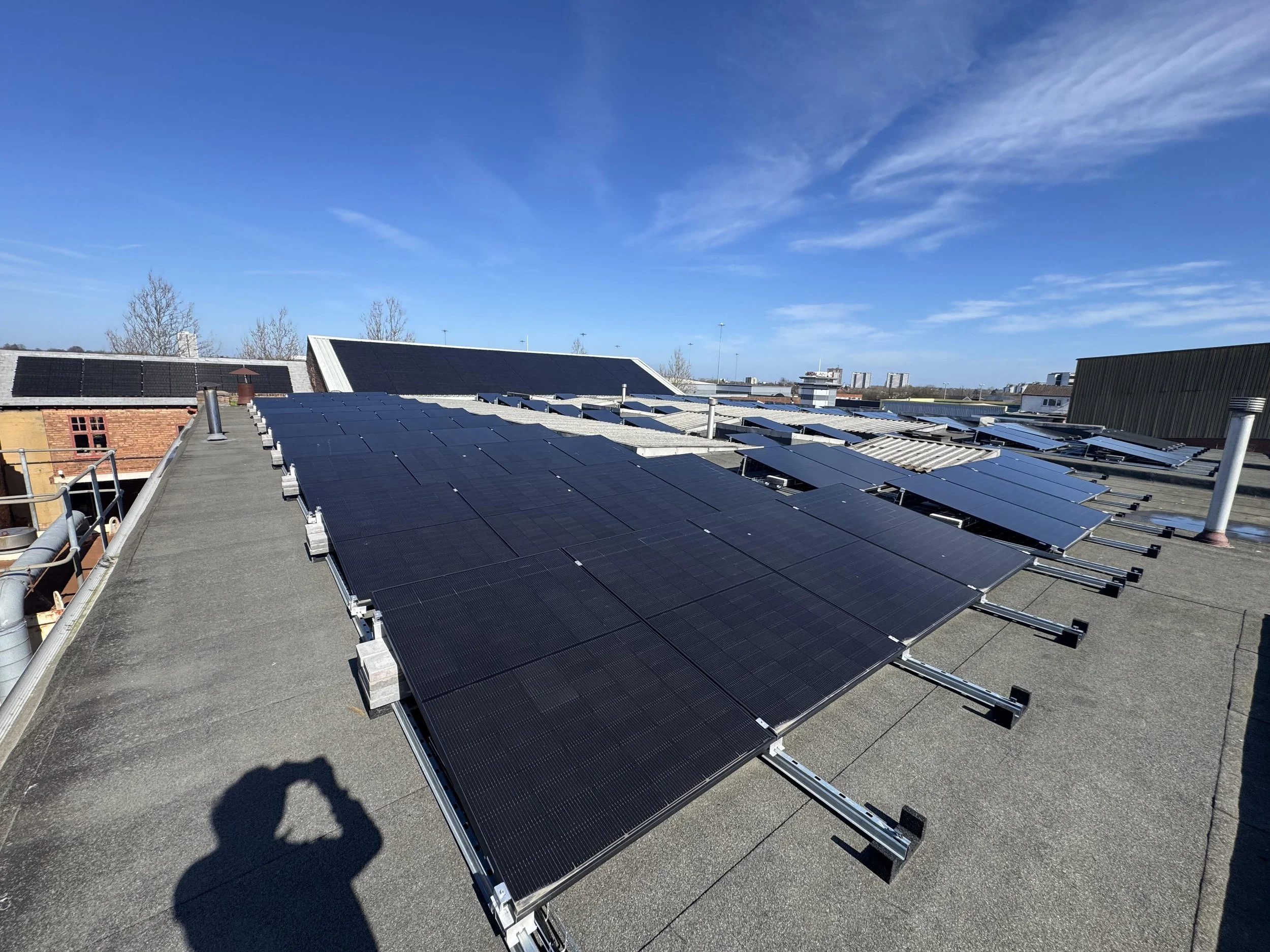 Multiple rows of solar panels installed on rooftops under a clear blue sky.