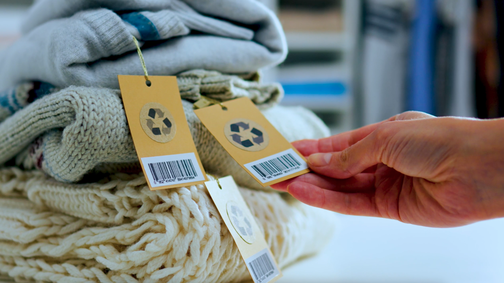 Palma di mani che stringono etichette di riciclo su pile di maglioni in tessuti vari.