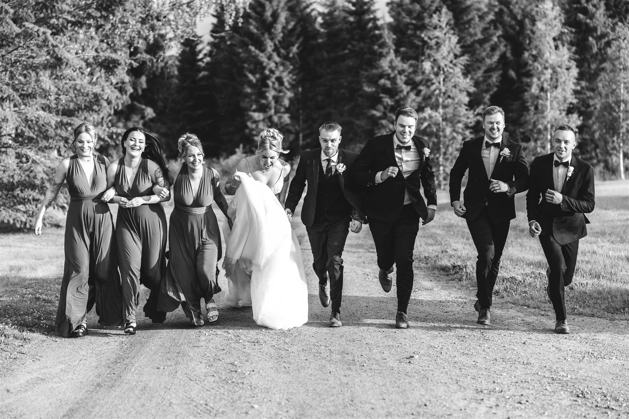 Vihreänä puistona ja tieosuuksina kulkeva, ryhmä hymyileviä ihmisiä juhlapuvussa kävelee yhdessä.
