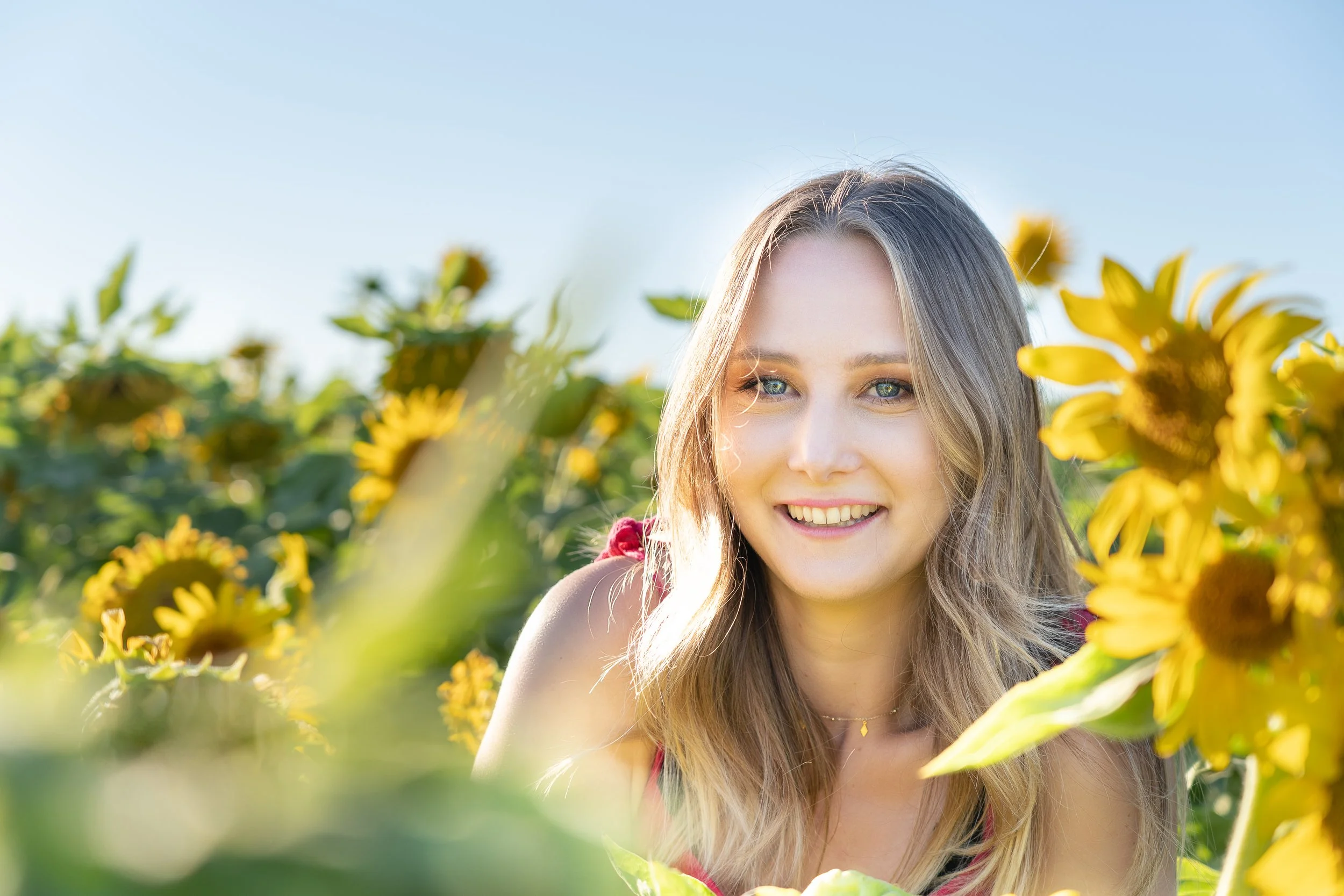 Jeune femme souriante dans un champ de tournesols sous un ciel bleu.