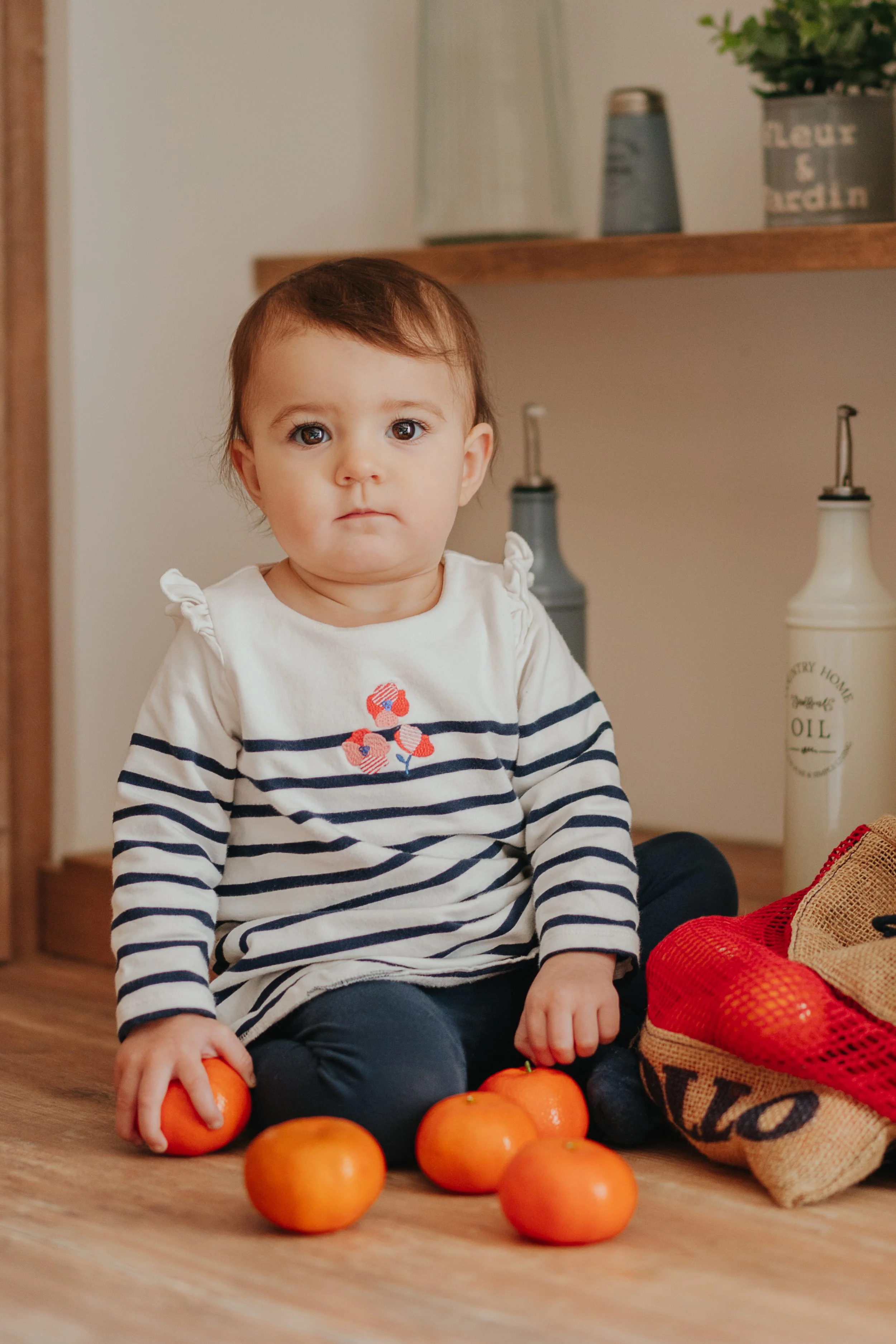 Un enfant assis par terre avec des clémentines et un sac en filet rouge à côté.