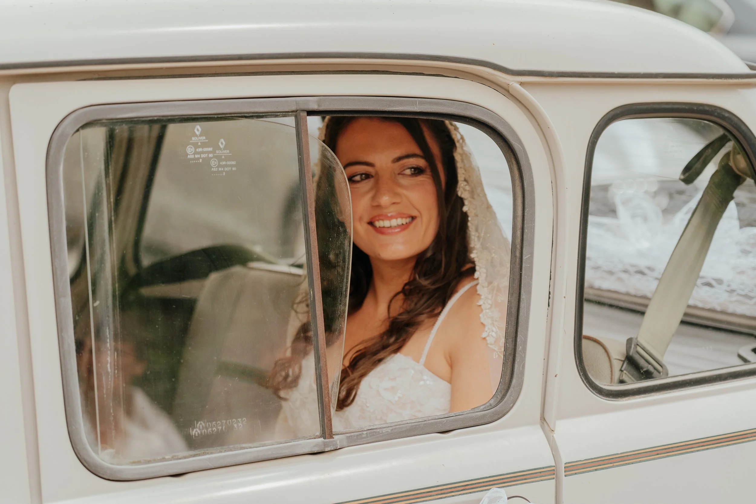 Une femme souriante avec une robe blanche, vue à travers la porte d'un sèche-linge sur une plage.