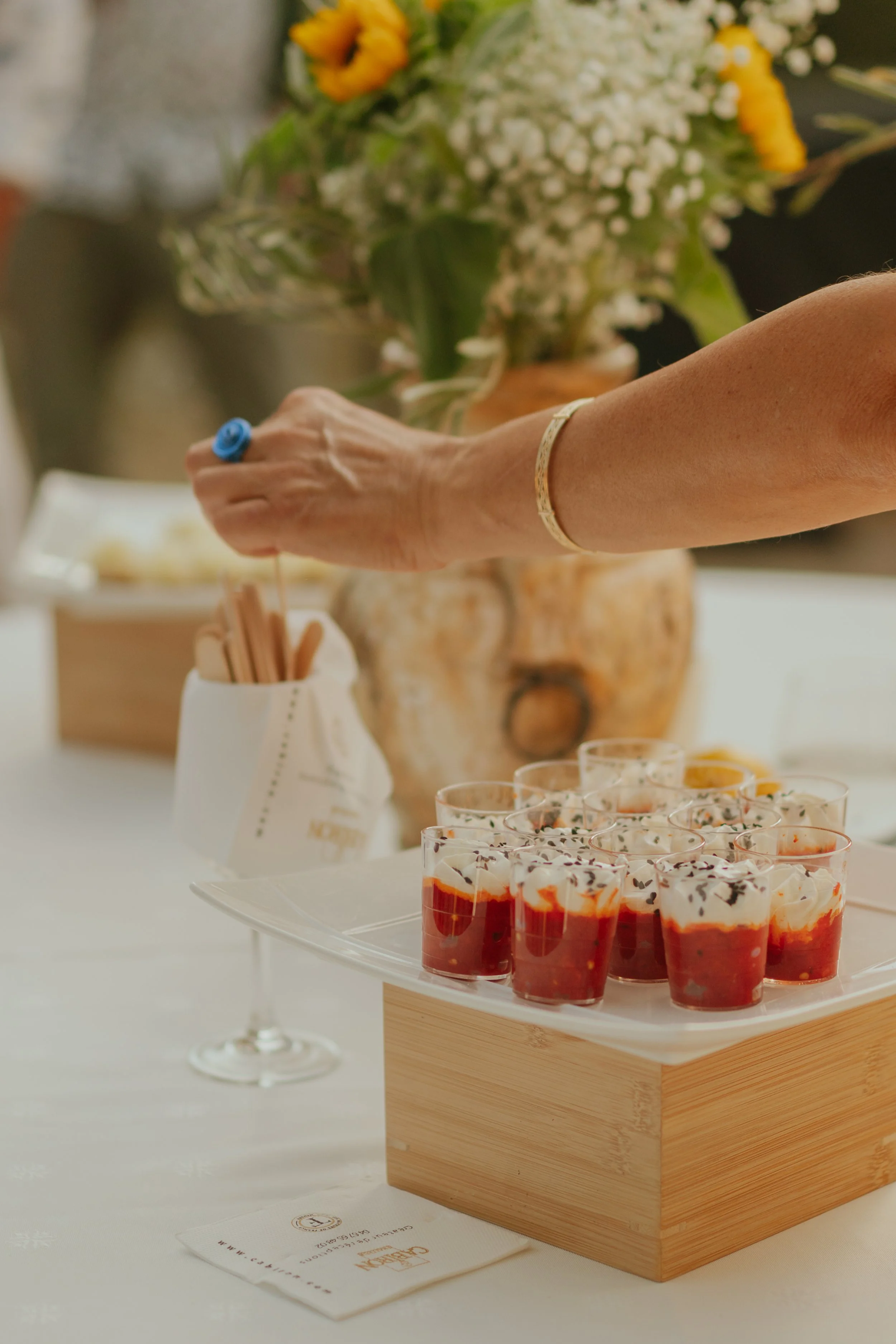 Gâteau de coupes en verrines de dessert aux fruits rouges, présenté sur un plateau en bois. En arrière-plan, un verre à vin et un bouquet de fleurs. Sur la table, un menu ou une carte de restaurant.