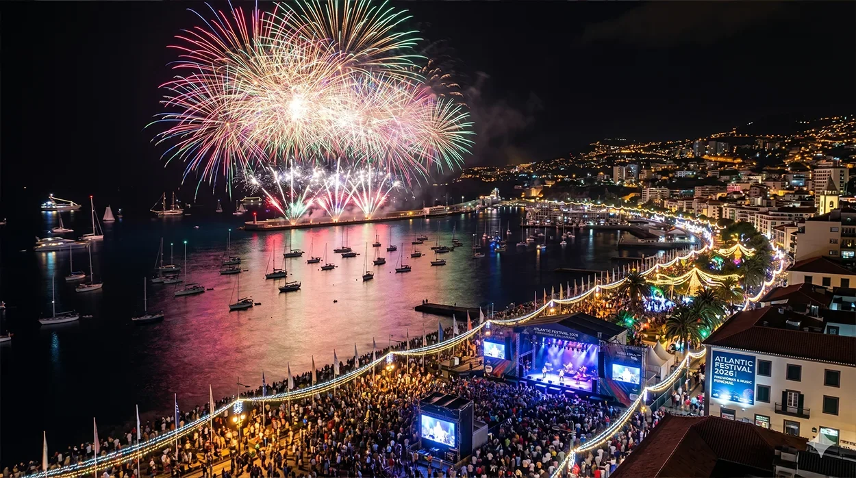 Fireworks bursting over Funchal Bay at night, with boats on the water and crowds along the lit seafront.