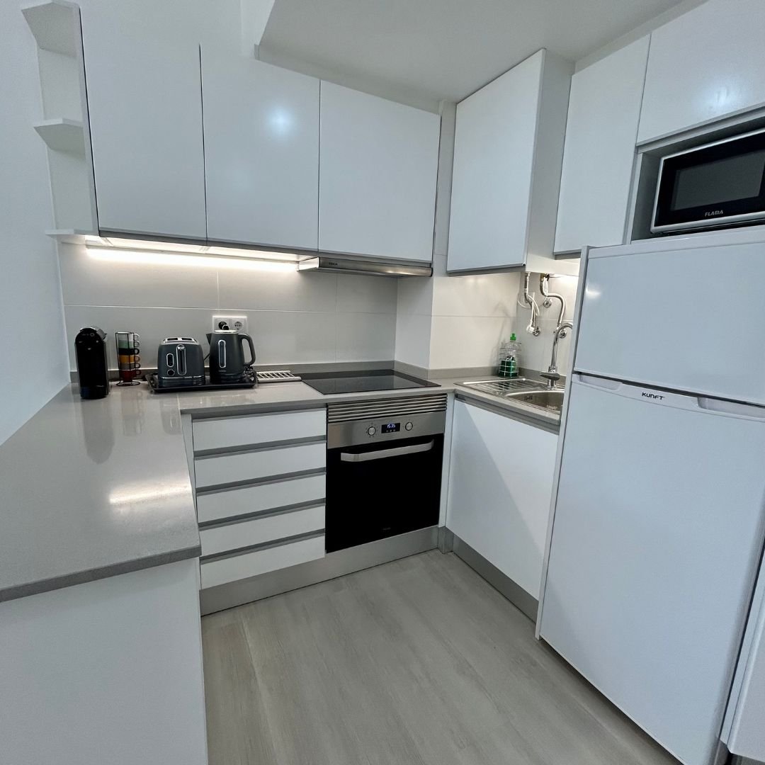 White fitted kitchen with an oven under an induction hob, a fridge freezer, microwave, toaster and coffee machine