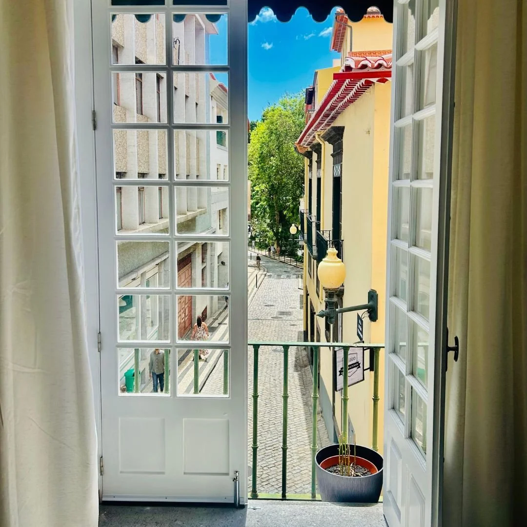 Open balcony doors looking down onto the cobbles of Rua da Carreira, with a yellow Madeiran facade opposite