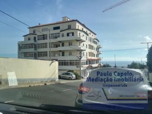 The block from the road, five white storeys standing above the coast with the sea behind it