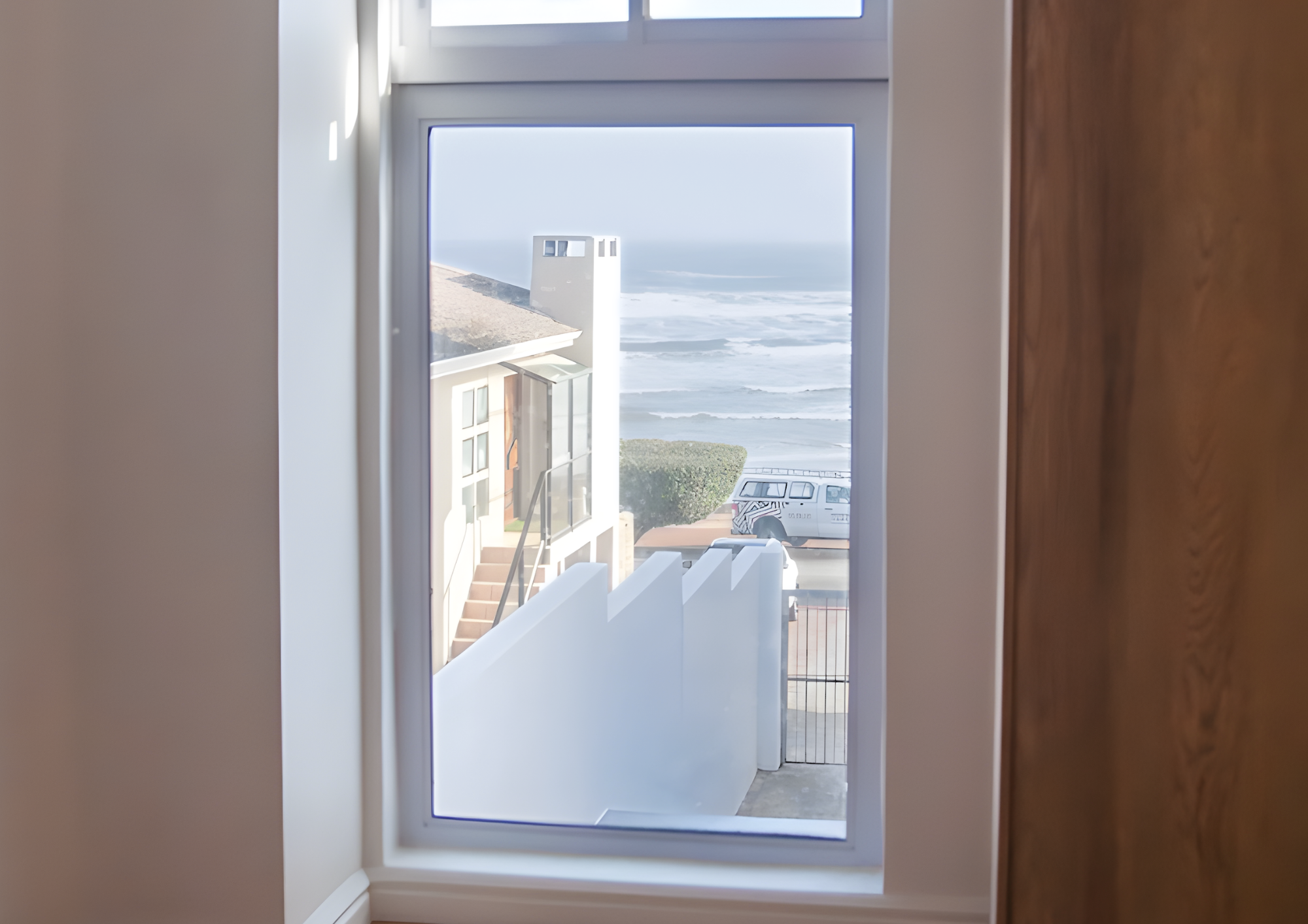 Modern white building under construction with large glass windows and door, construction materials on the ground, and a blue sky in the background.