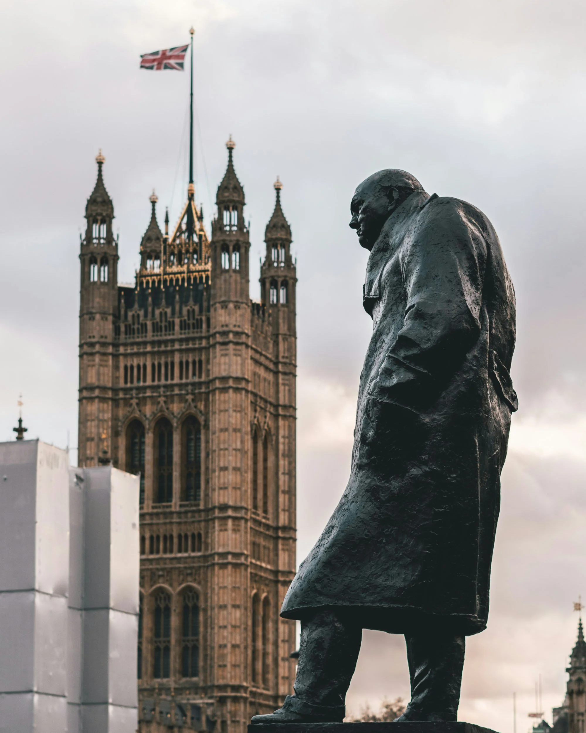 Bronze statue of Winston Churchill in front of the Palace of Westminster in London, England, with a cloudy sky.
