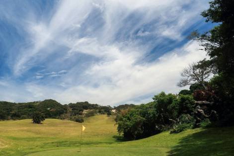 Port St Johns Golf Club, with a green, flagstick, trees, and blue sky with clouds