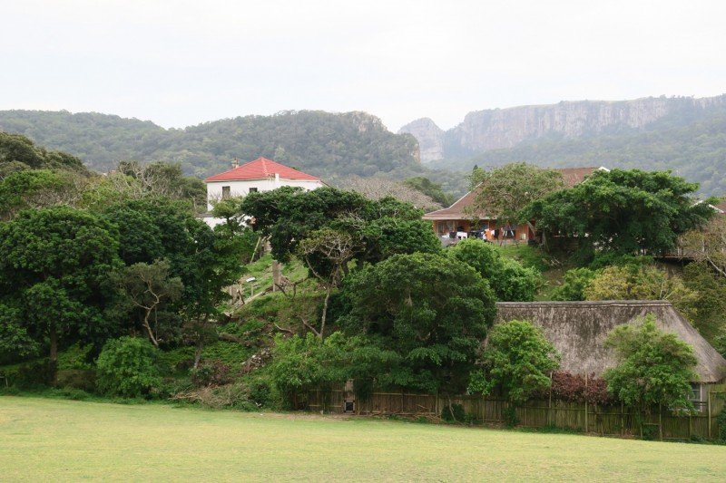 Scenic landscape featuring houses among lush green trees with mountains in the background.