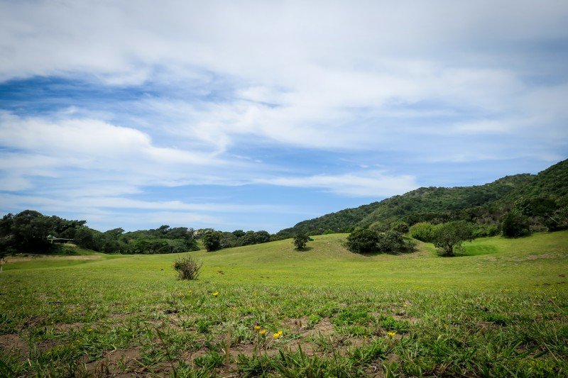 Port St Johns Golf Club, with trees and hills under a partly cloudy sky.
