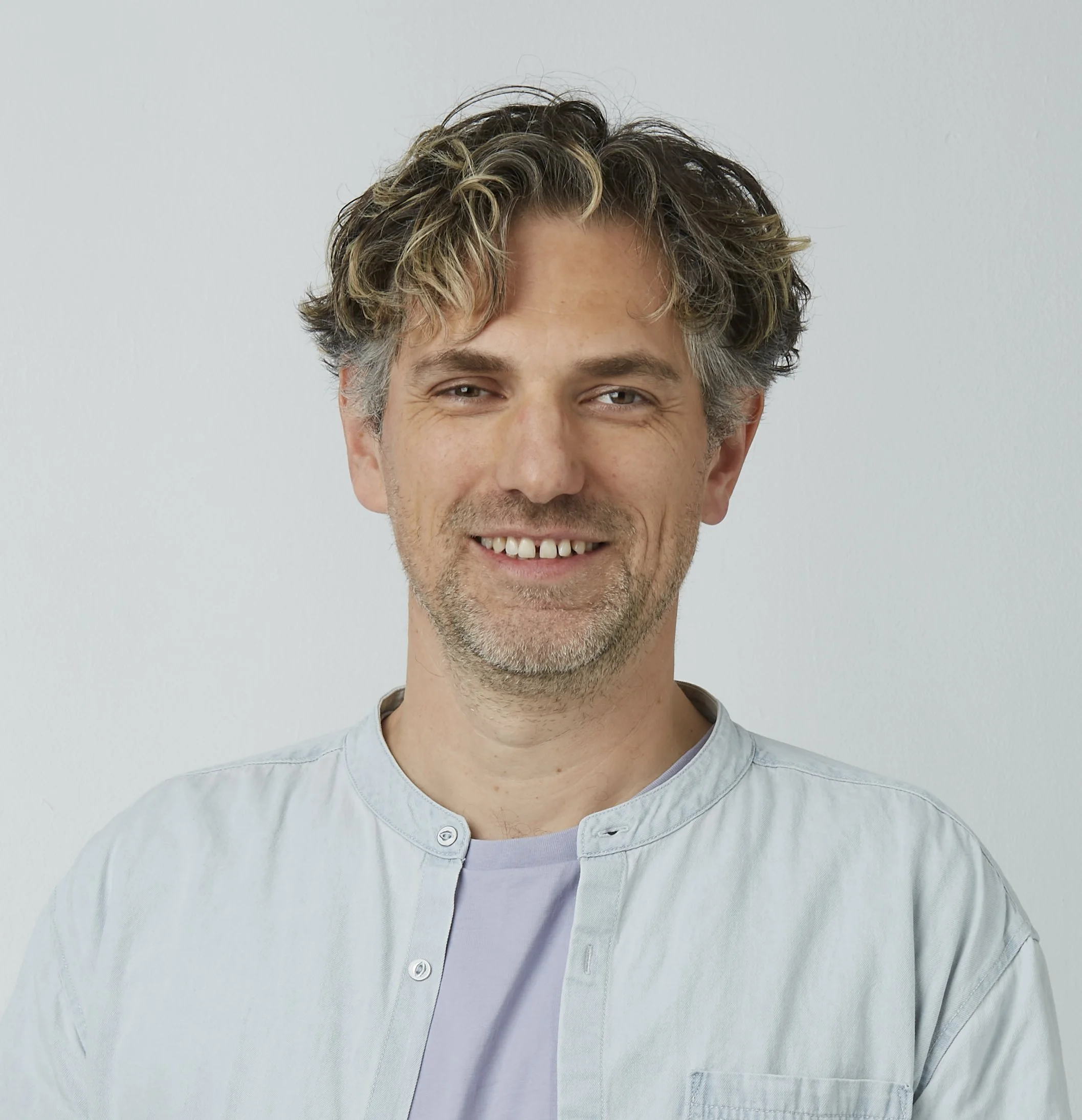 Der integrale Coach & Organisationsentwickler Dr. med. Jonas Westphal schaut lächelnd in die Kamera. Er trägt ein offenes helles Jeanshemd und ein fliederfarbenes T-Shirt.