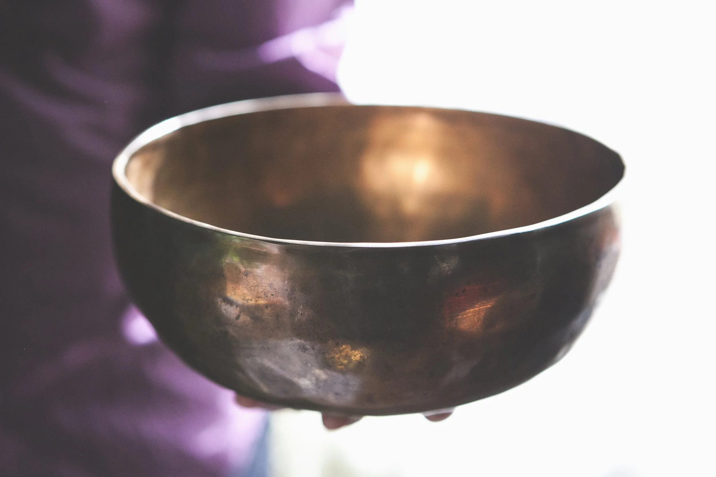 A Himalayan singing bowl with a dark, tarnished surface, with the background bright and blurry.