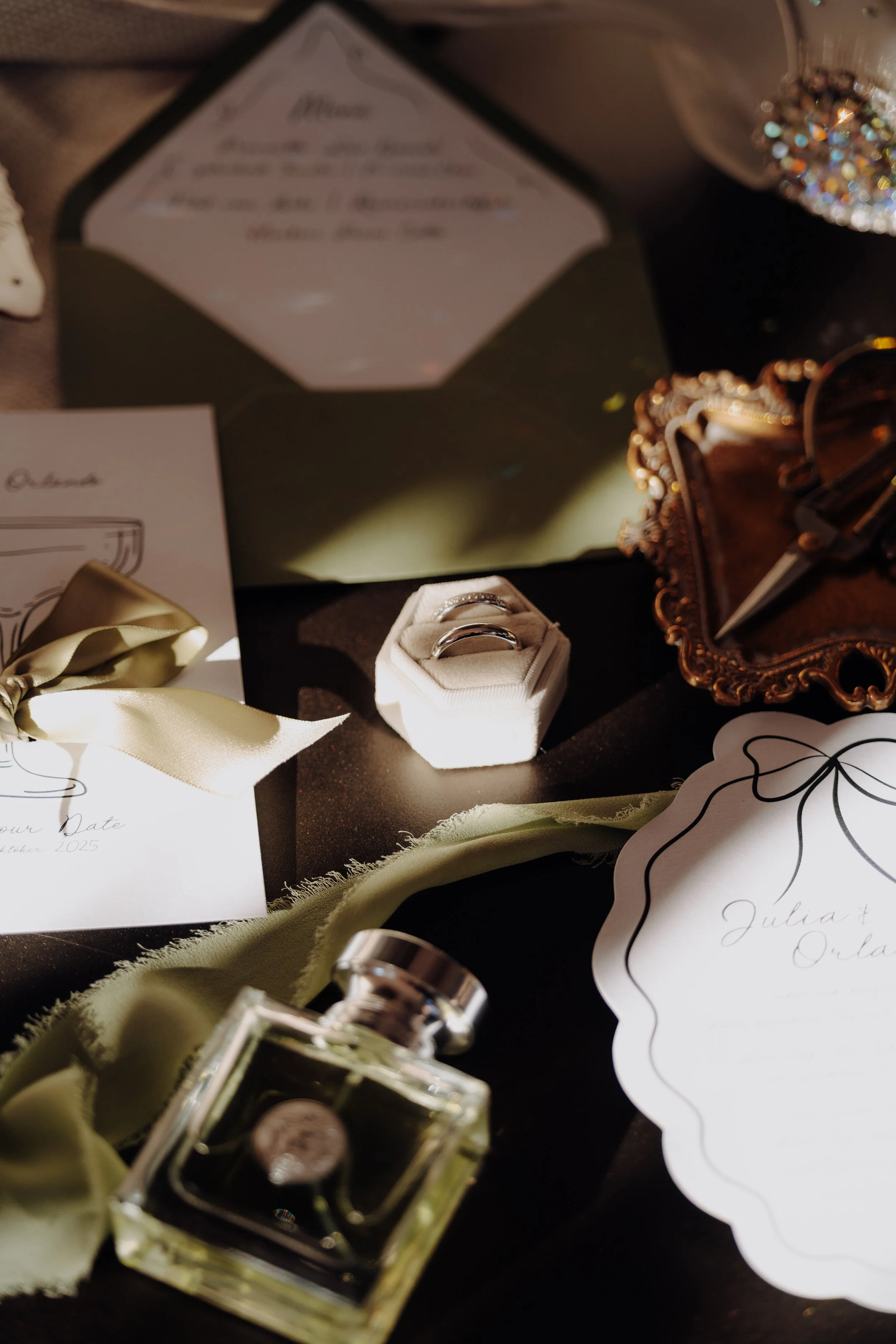Auswahl von Hochzeitsaccessoires, darunter Eheringe, ein Parfümflakon, Blumendekoration, Einladungskarten, und ein Ziergegenstand mit funkelnden Steinen.