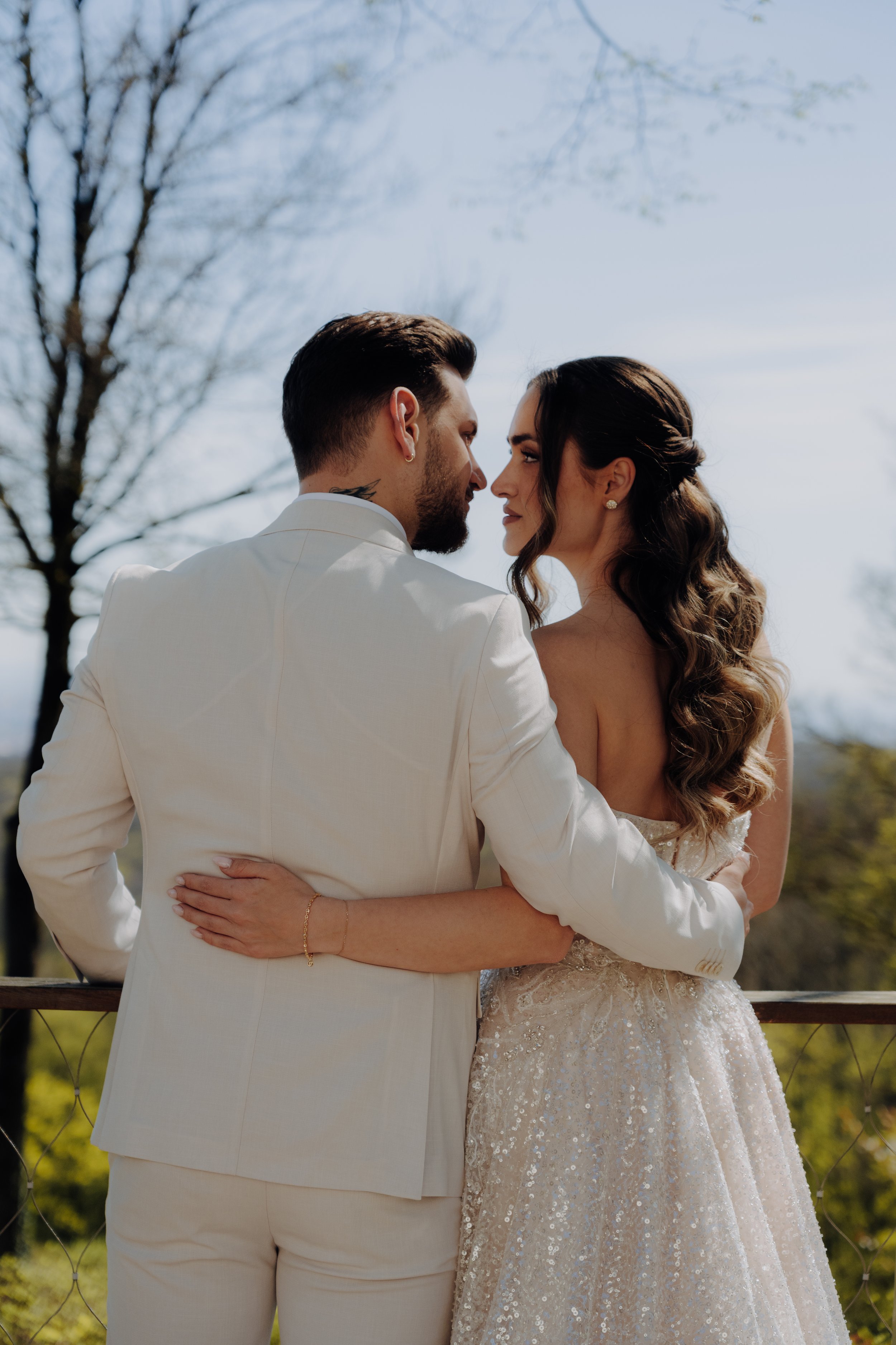 Ein Paar in Hochzeitskleidung, das sich an einem sonnigen Tag im Freien liebevoll ansieht.