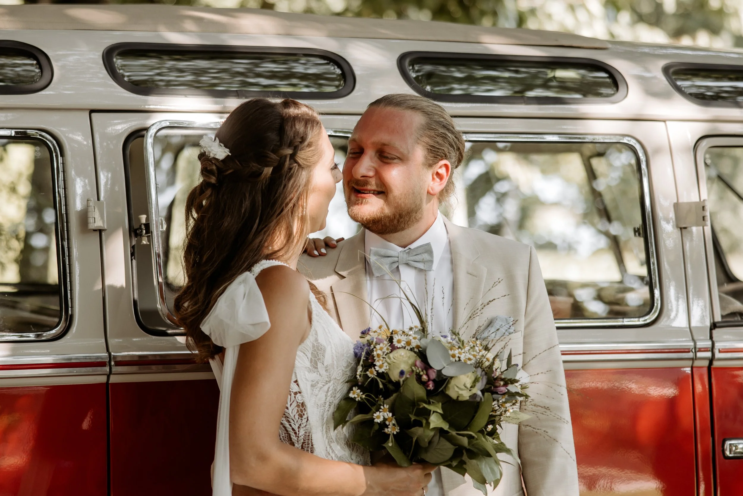 Ein Brautpaar steht vor einem nostalgischen roten und weißen Oldtimer, lächelnd und in Liebe vereint, bei Hochzeit.