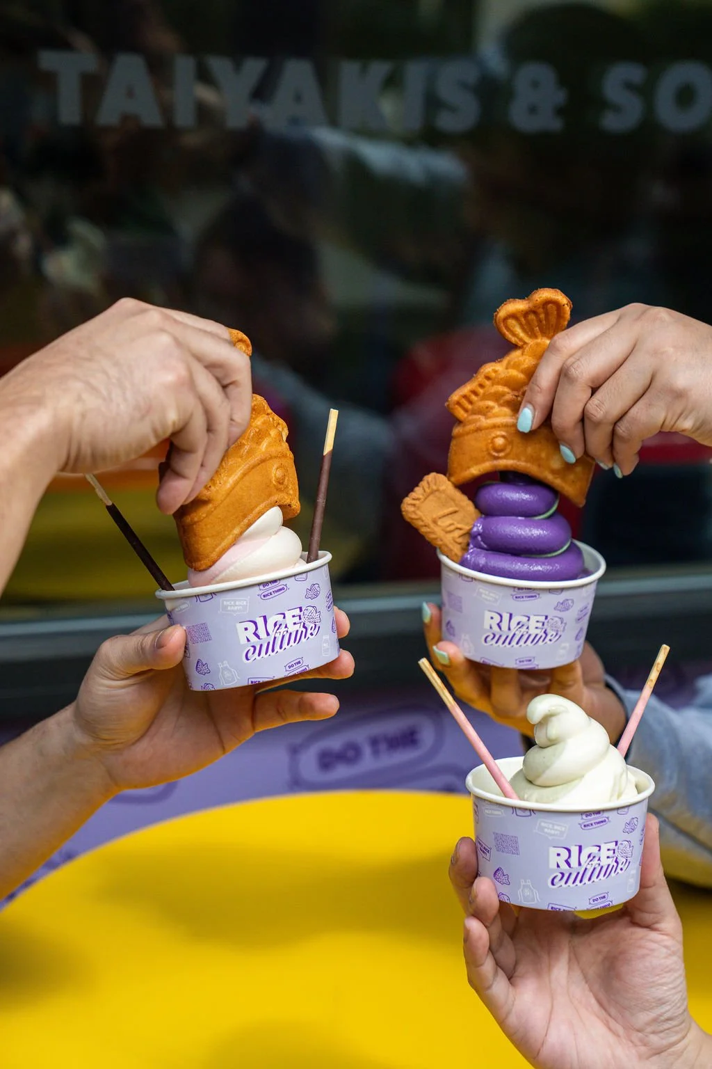 Three people holding cups with ice cream and fish-shaped waffle toppings