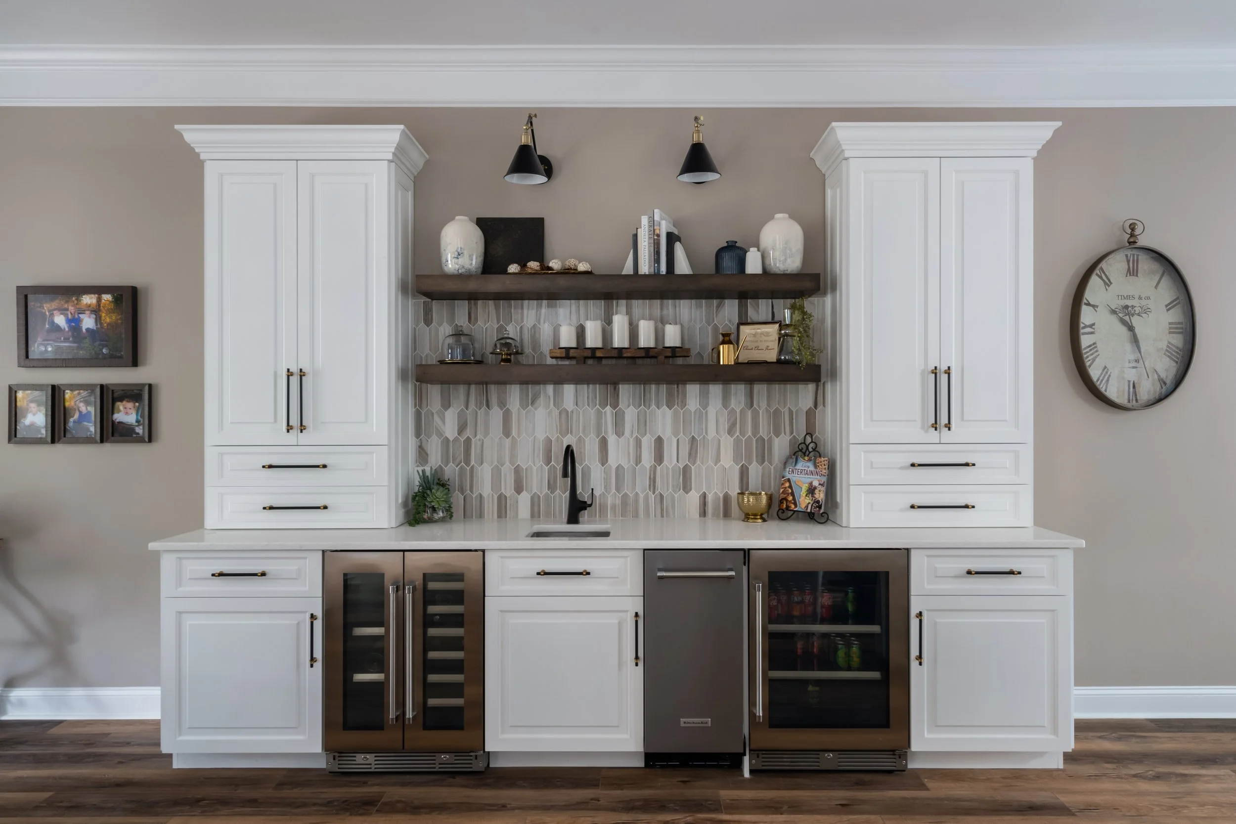 A built-in bar area with white cabinetry, floating wood shelves, and a patterned backsplash, flanked by beverage coolers.