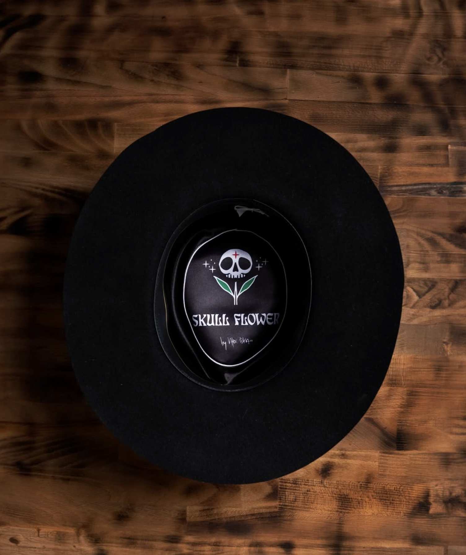 Black hat with a label inside displaying a skull with leaves and the text 'Skull Flower' on a wooden surface.
