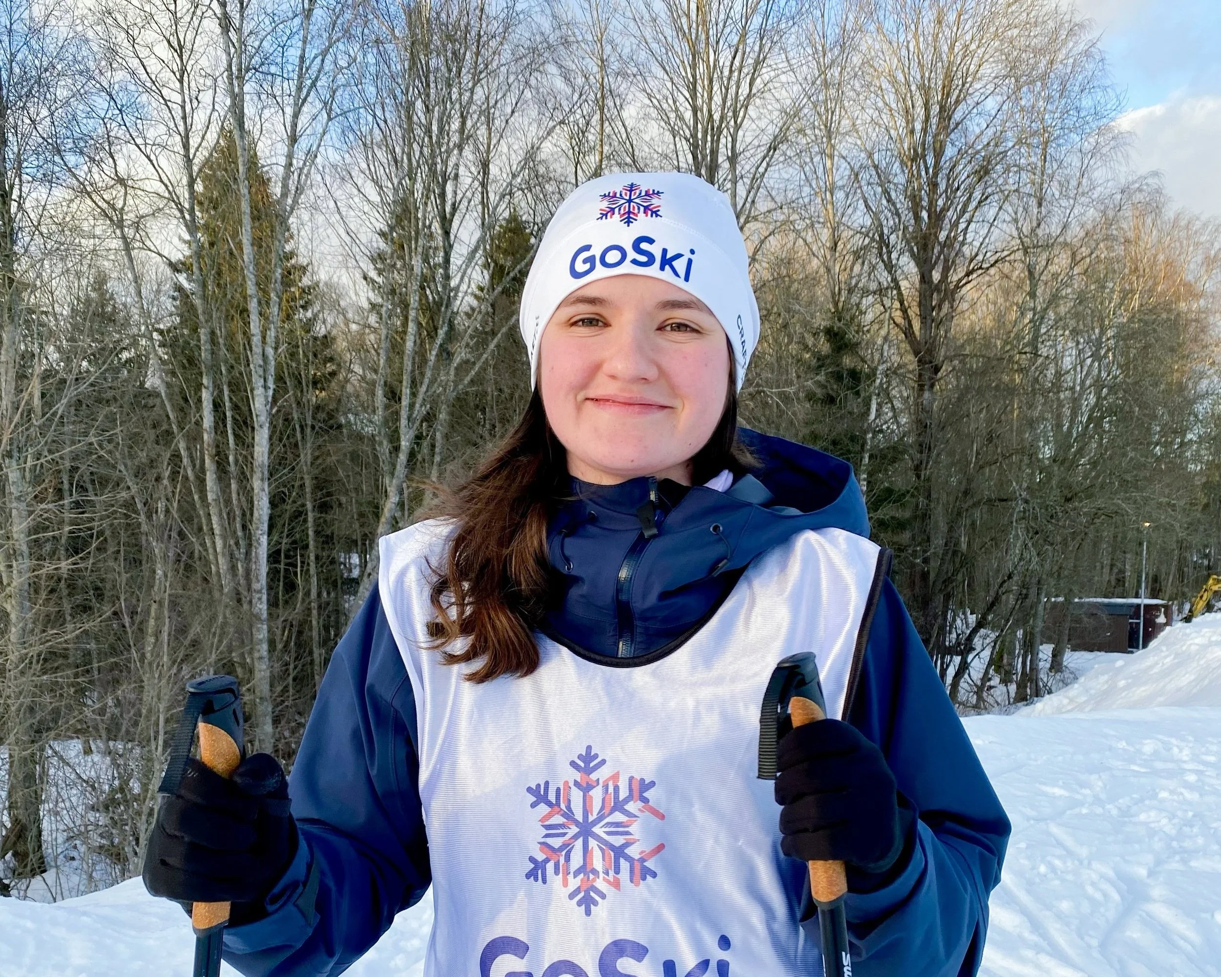 A ski instructor wearing a hat with GoSki logo and smiles in the camera