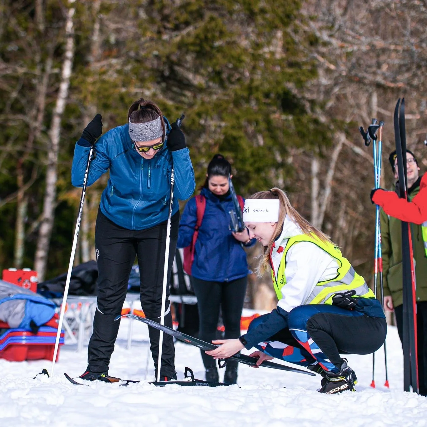 Female instructor helps with ski bindings for woman in blue jacket