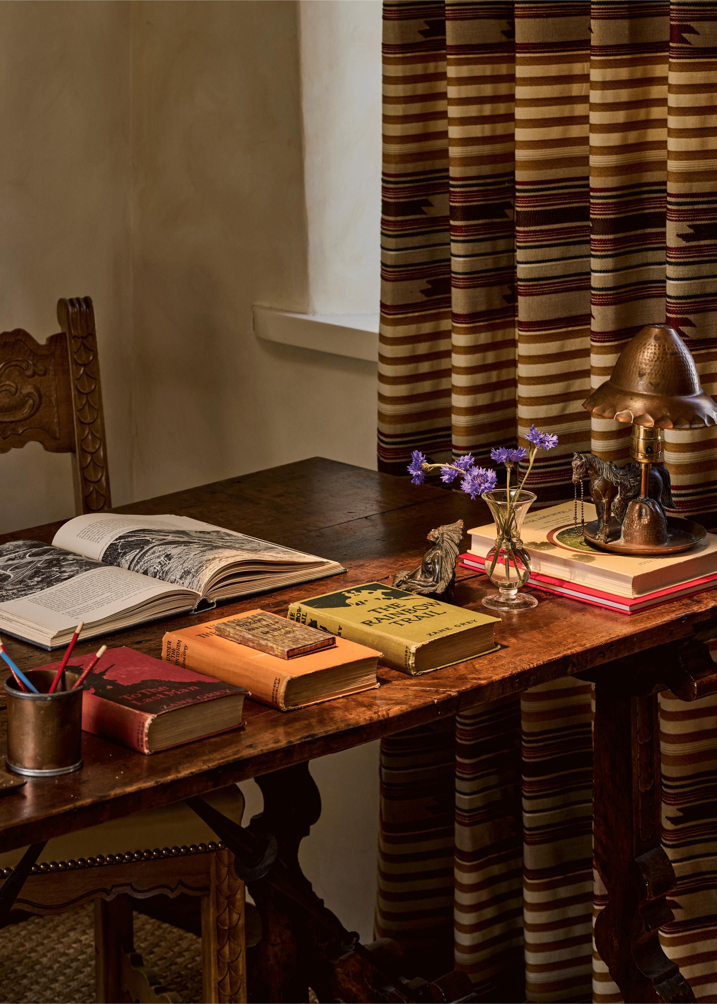 A closer view of the Mesa Project's study desk: vintage volumes, a hammered copper lamp, and Southwest-stripe drapes that blur the line between collected and designed. French & French Interiors stages objects the way a good editor places words - noth