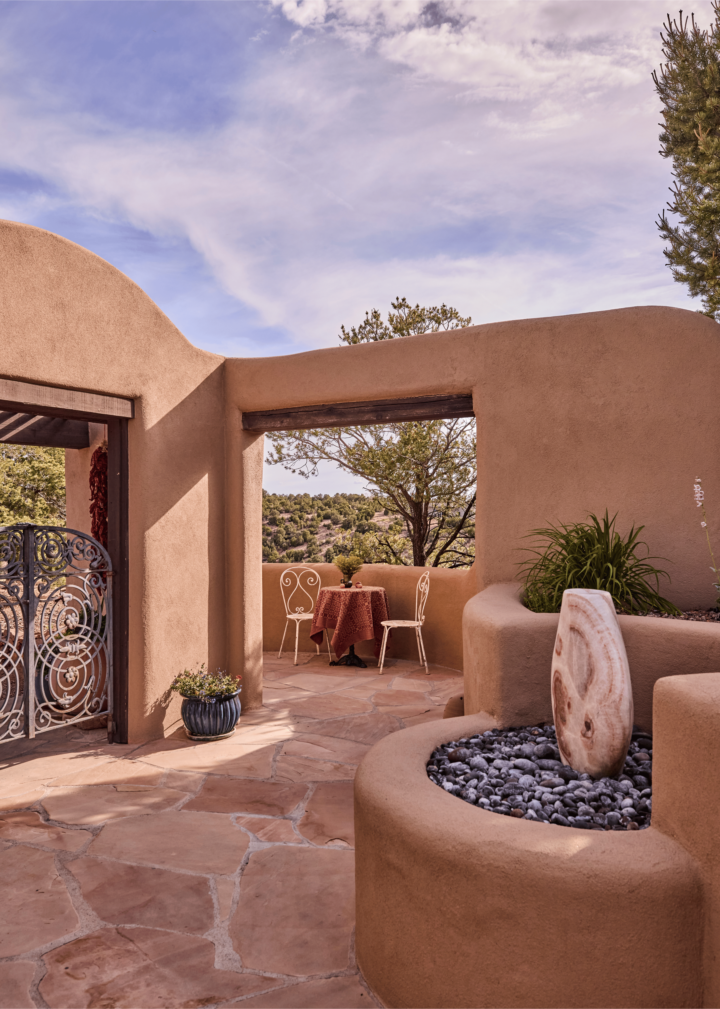 The transition between interior and exterior at the Mesa Project is seamless - flagstone paving, adobe walls, a carved stone water feature, and a terrace framing the desert beyond. Exterior and landscape details by French & French Interiors, Tesuque,