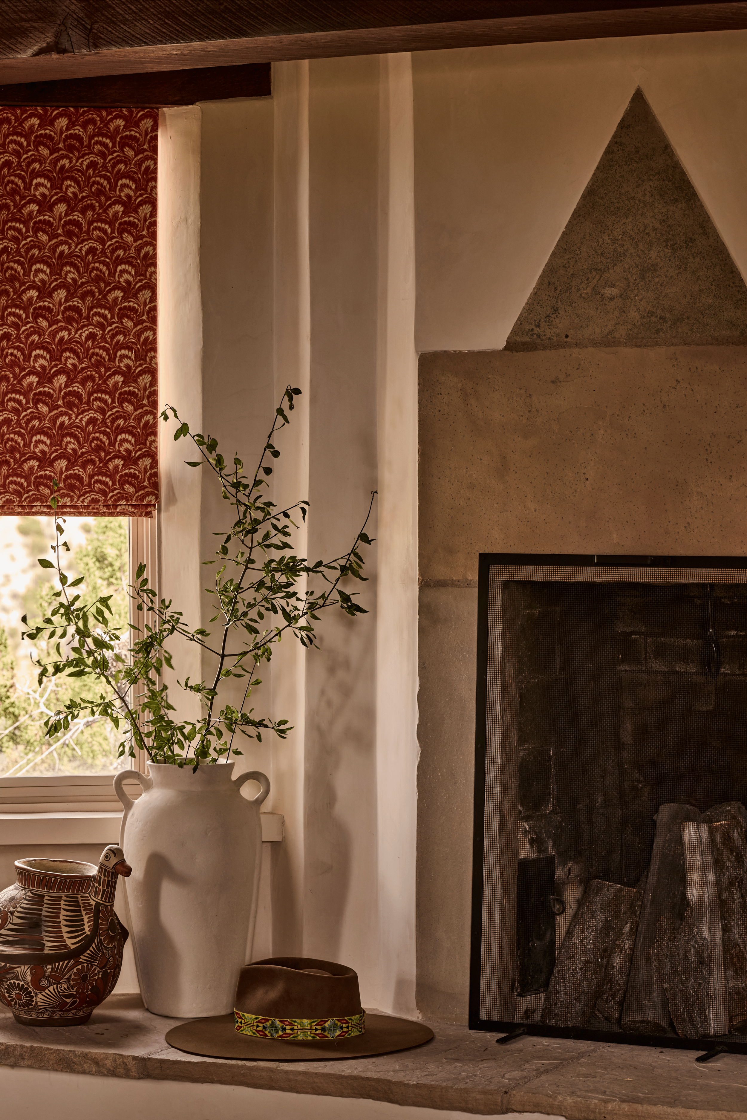 The Mesa Project's fireplace hearth is styled with a white ceramic vase, a folk-art clay bird, and a felt hat resting on carved stone - small, considered details that give French & French Interiors' work its sense of lived-in authenticity rather than