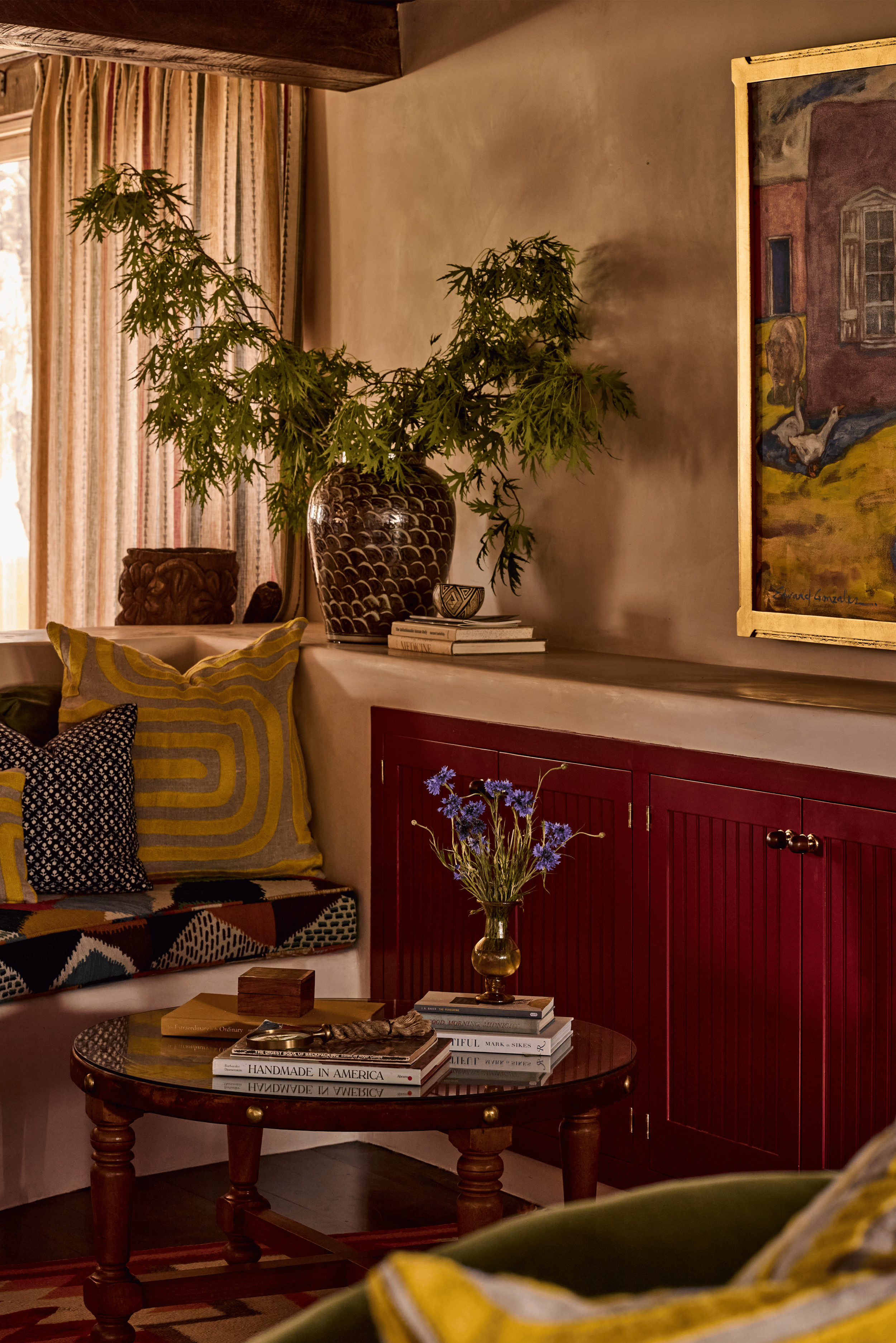Deep red built-in cabinetry, a mustard geometric pillow, and a dark ceramic vase layered against a gold-framed oil painting - this living room vignette at the Mesa Project captures exactly how French & French Interiors layers color and art to create 