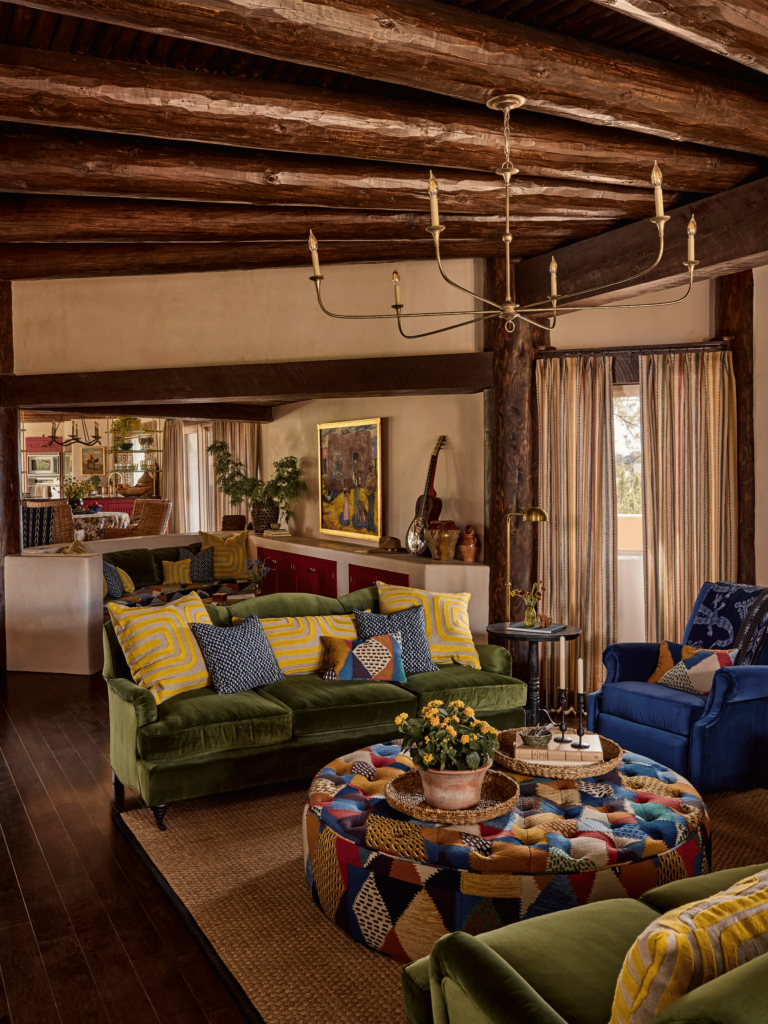 The main living room of the Mesa Project in full: forest green velvet, a patchwork kilim ottoman, navy club chairs, and a New Mexico landscape painting above the fireplace. French & French Interiors designed this room as a lodge-style gathering space