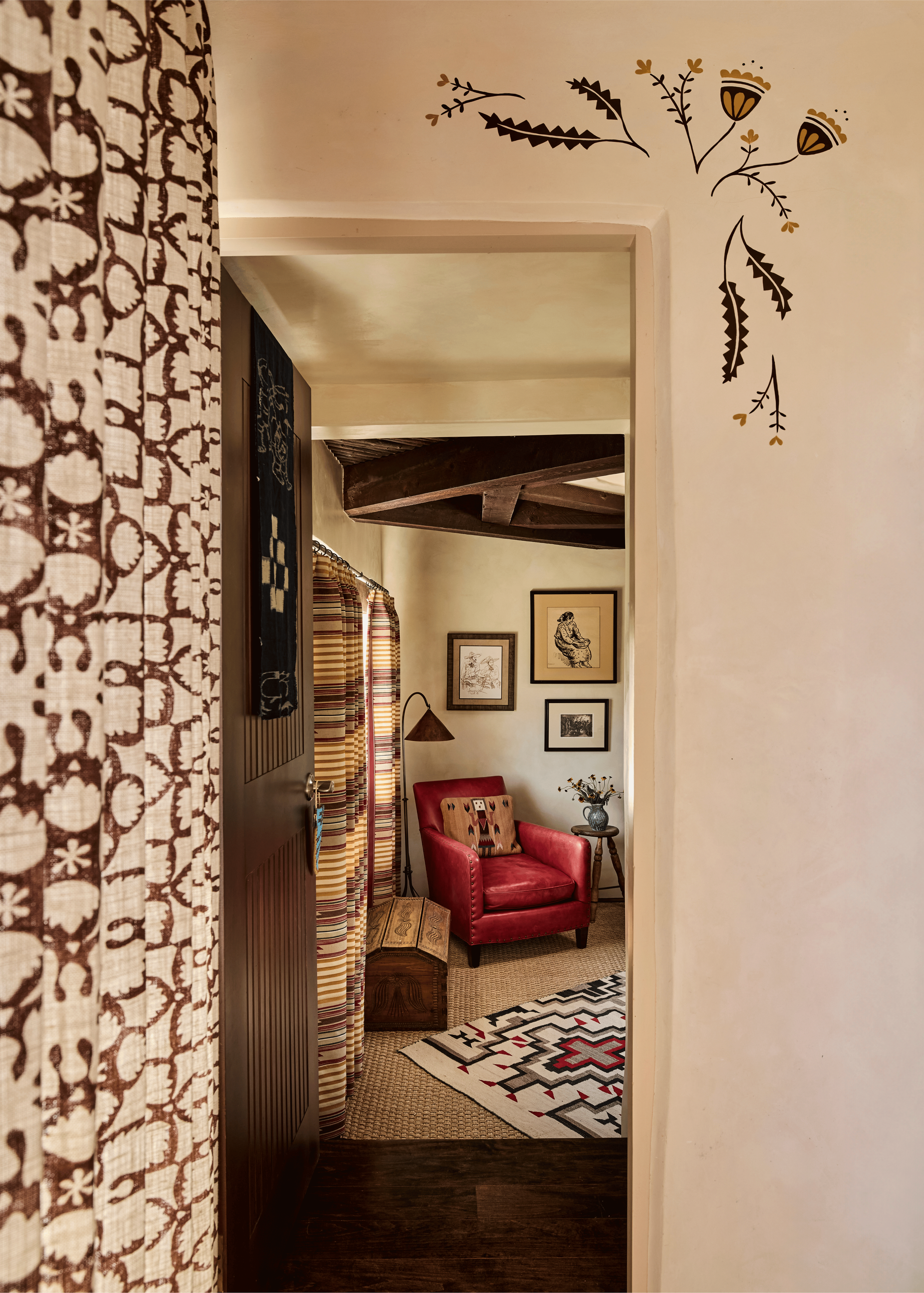 From this angle, the hand-painted botanical detail at the Mesa Project reads as a full decorative moment - gold and black folk motifs floating above the doorway, with a red leather chair and Navajo-print rug visible in the den beyond. French & French